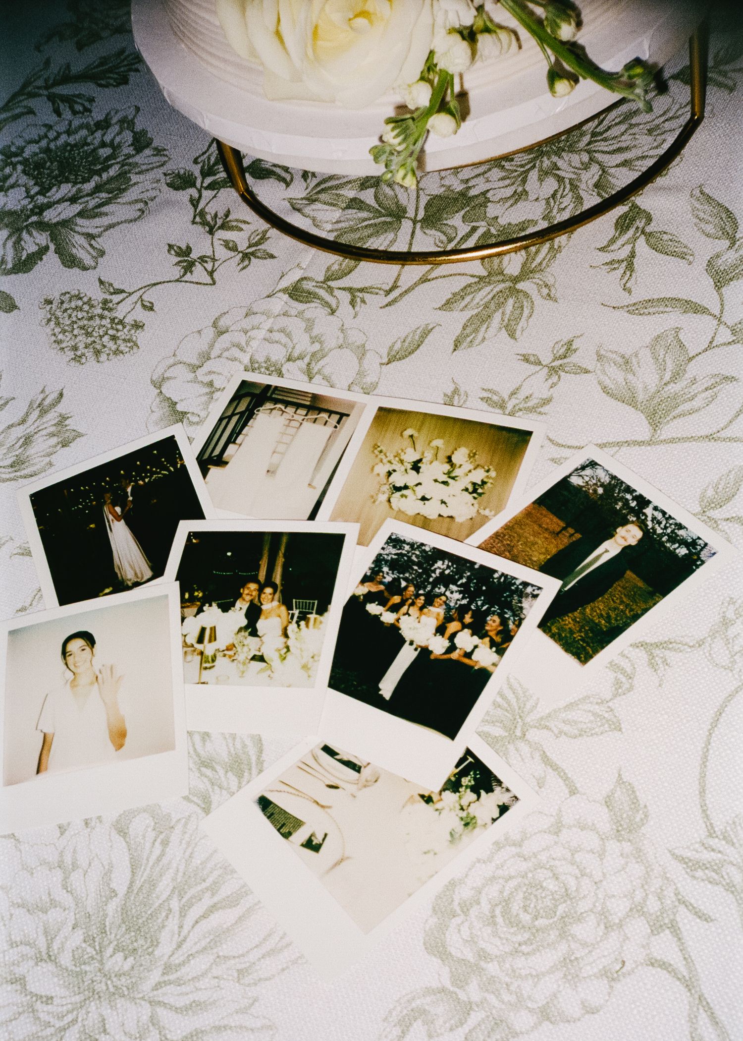 Wedding photos and memorabilia arranged on a white floral patterned tablecloth.