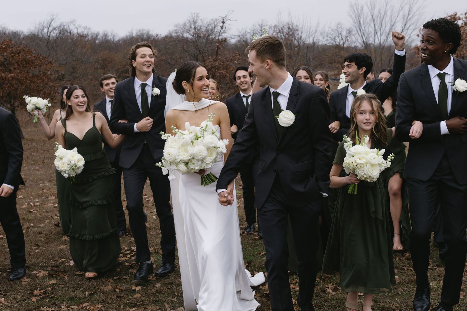 Wedding party walks together outdoors in black and white formal attire.