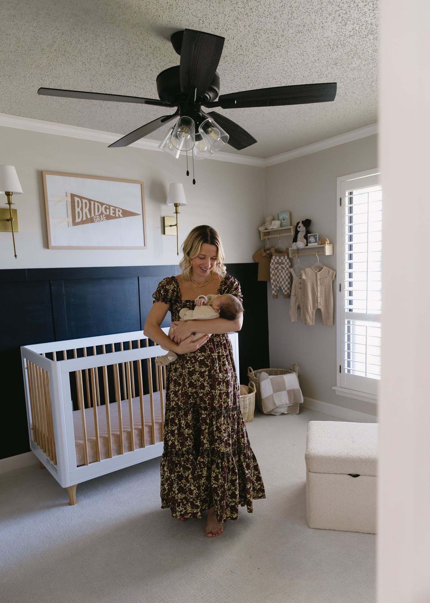 A nursery room with modern decor featuring a white crib, ceiling fan, and floral dress details.