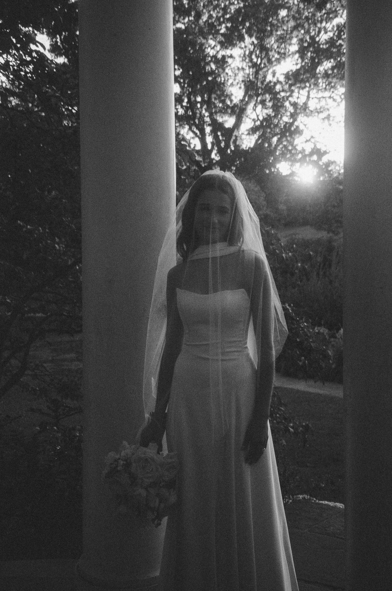 A silhouetted figure in a flowing dress stands between white columns at sunset creating a dreamy ethereal effect.