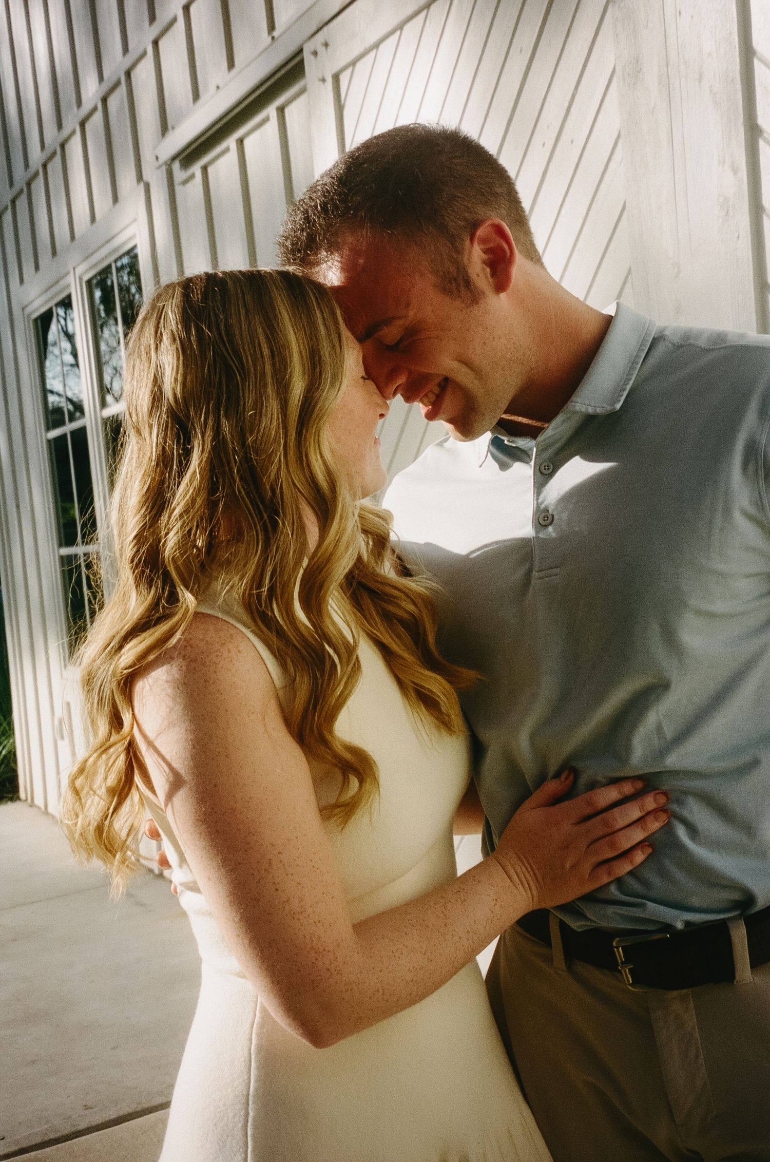 A tender moment captured between a couple on a bright white porch during a photo session.