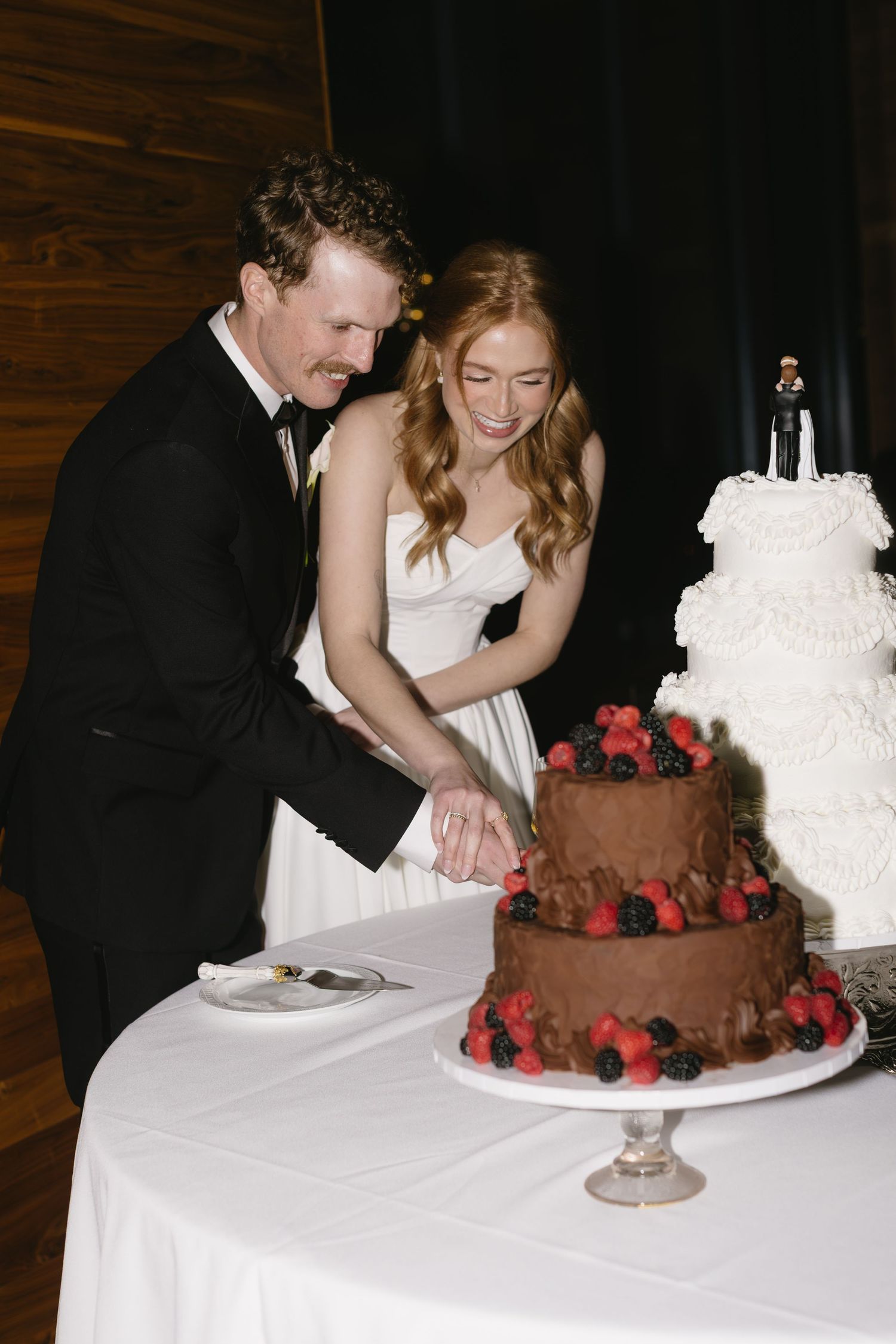 Wedding couple cutting their chocolate and white tiered wedding cake decorated with berries.