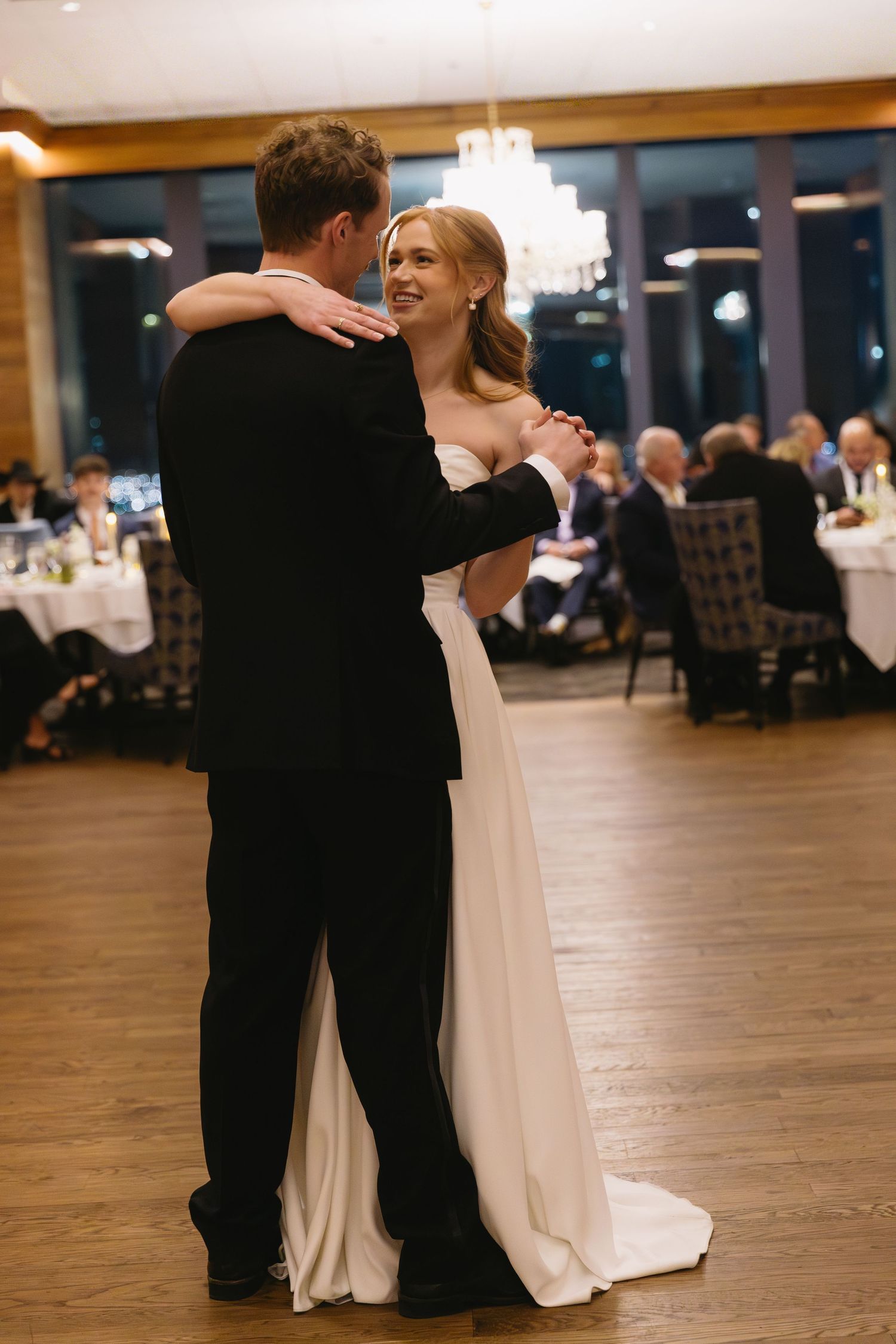 Couple sharing their first dance on a wooden floor at their wedding reception.