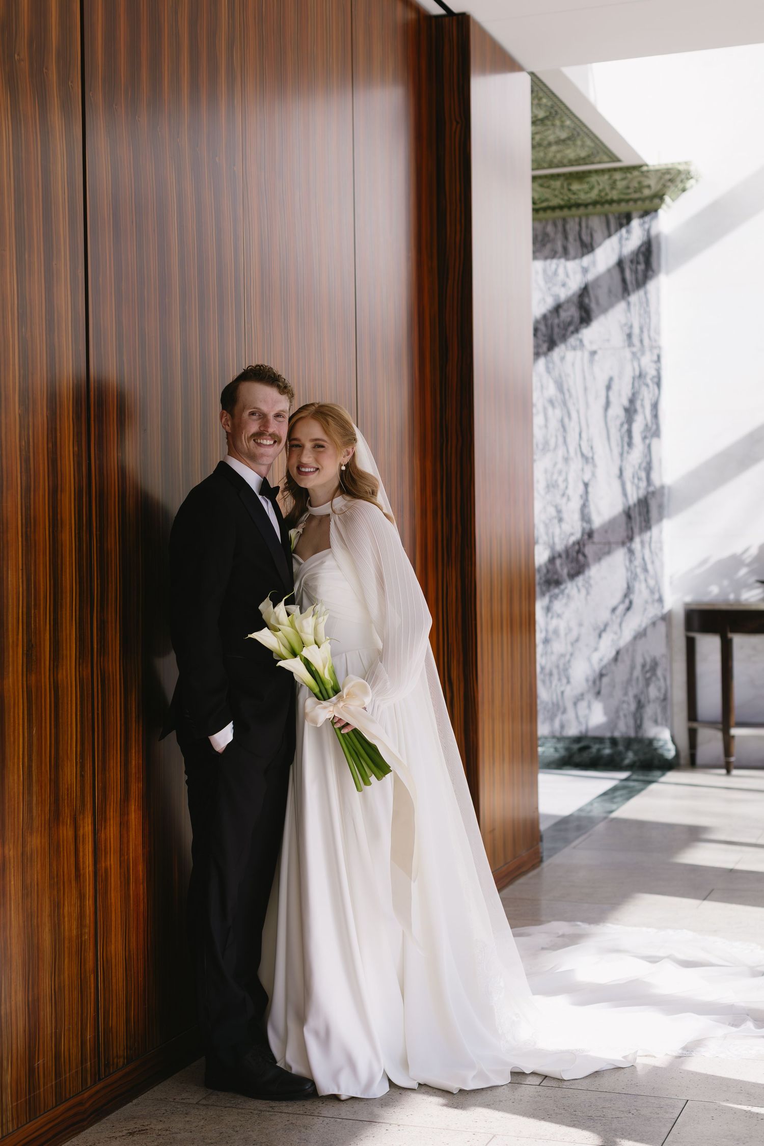A romantic wedding moment captured in an elegant wood-paneled hallway with natural light streaming in.