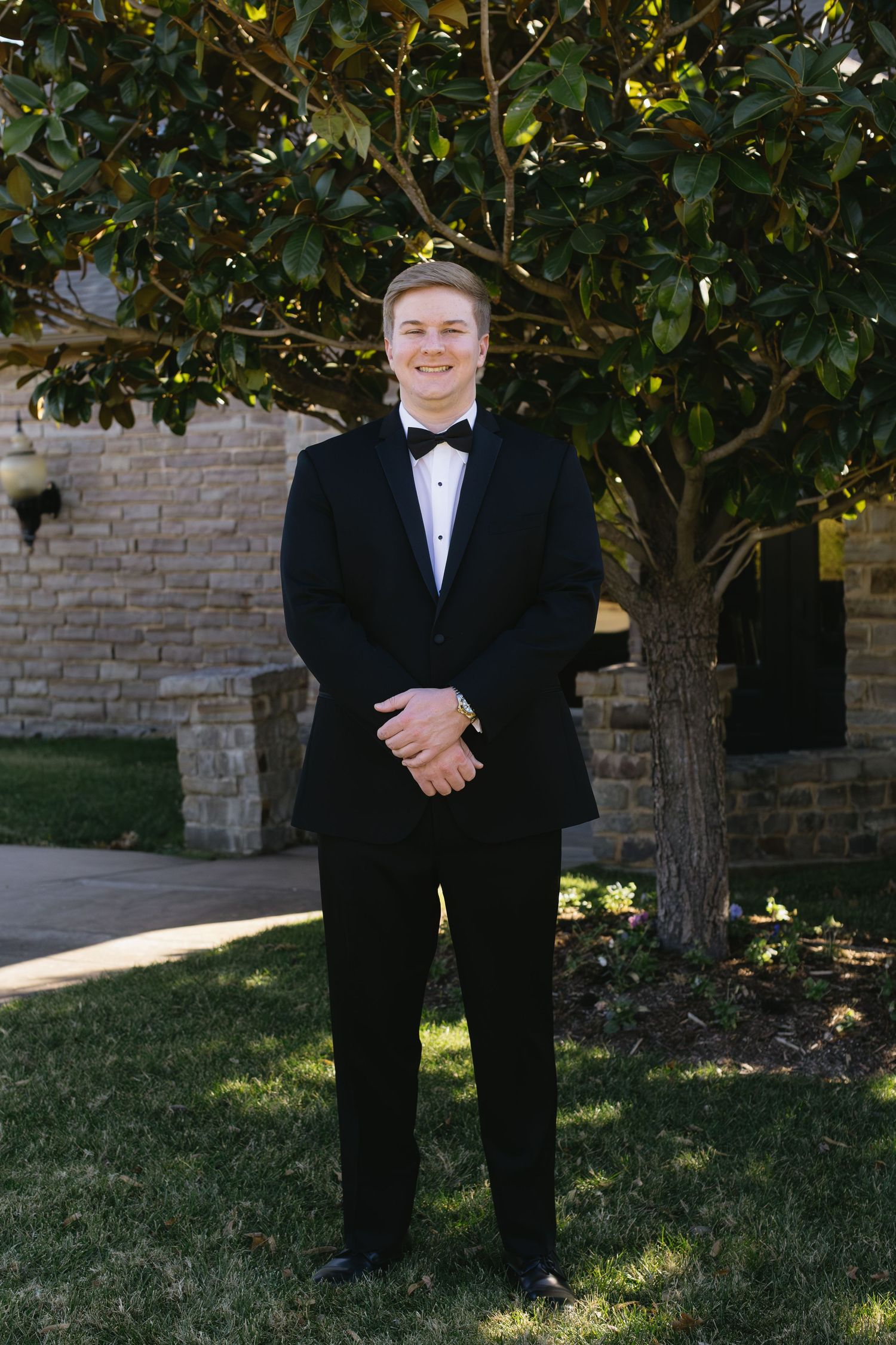 Formal wedding attire shown outdoors against a stone wall and green foliage.