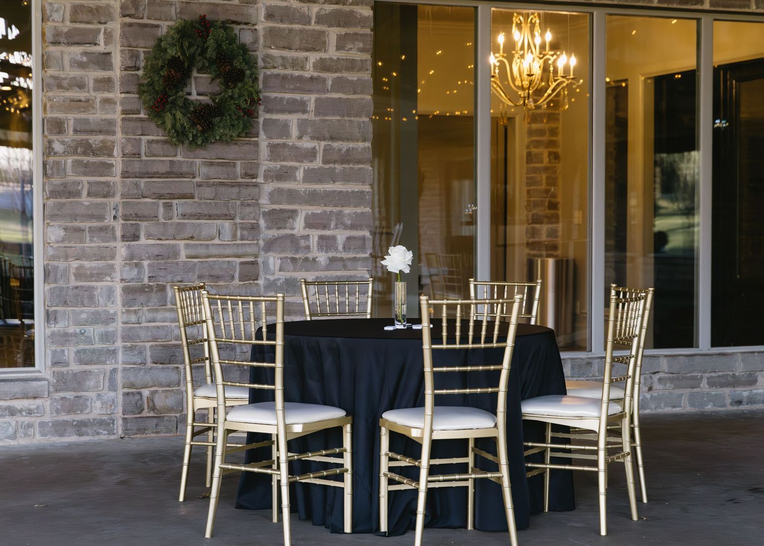 Stone exterior of venue with white chiavari chairs arranged on patio.
