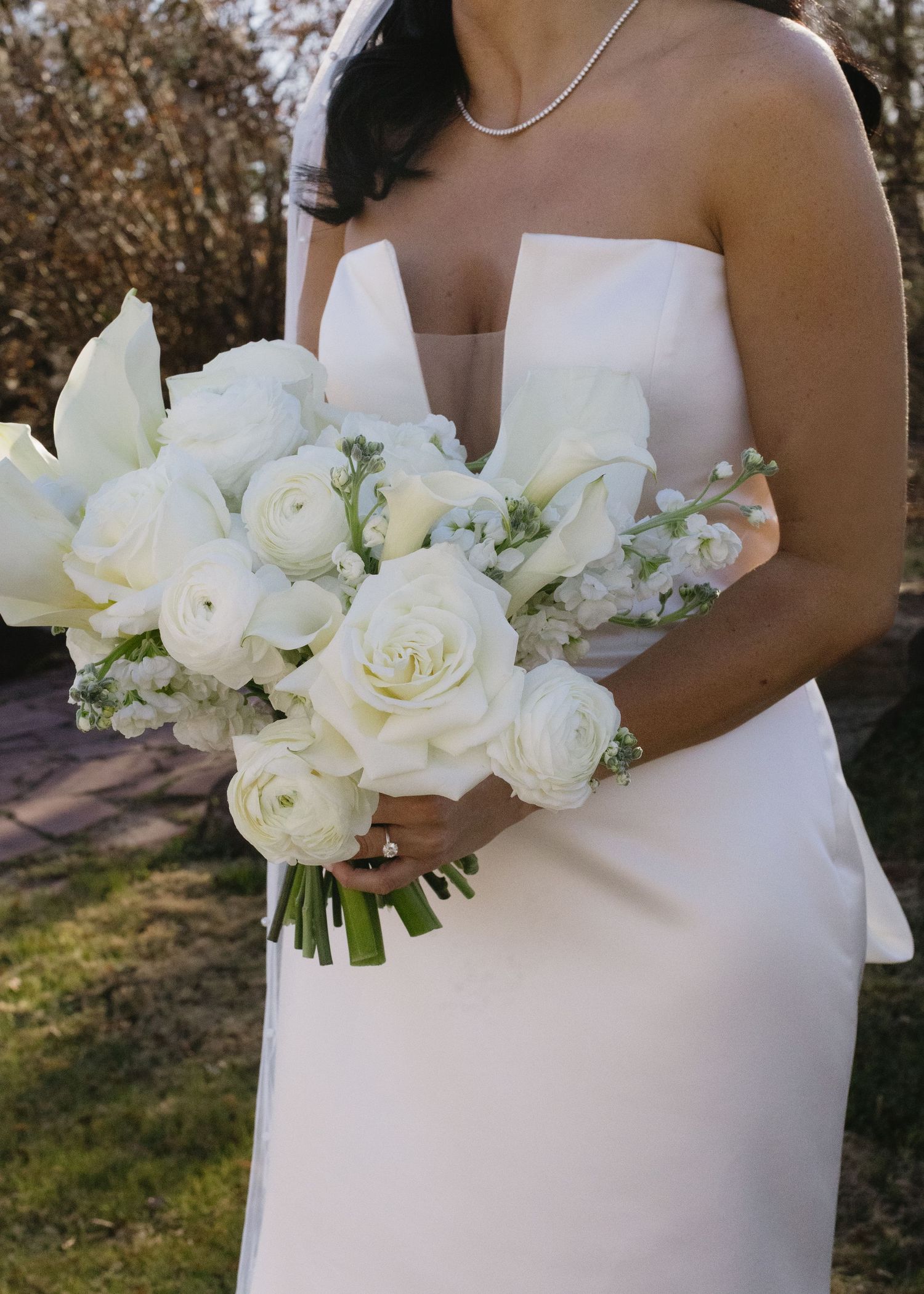 Bride holding a stunning white rose and ranunculus bouquet against a simple white dress.