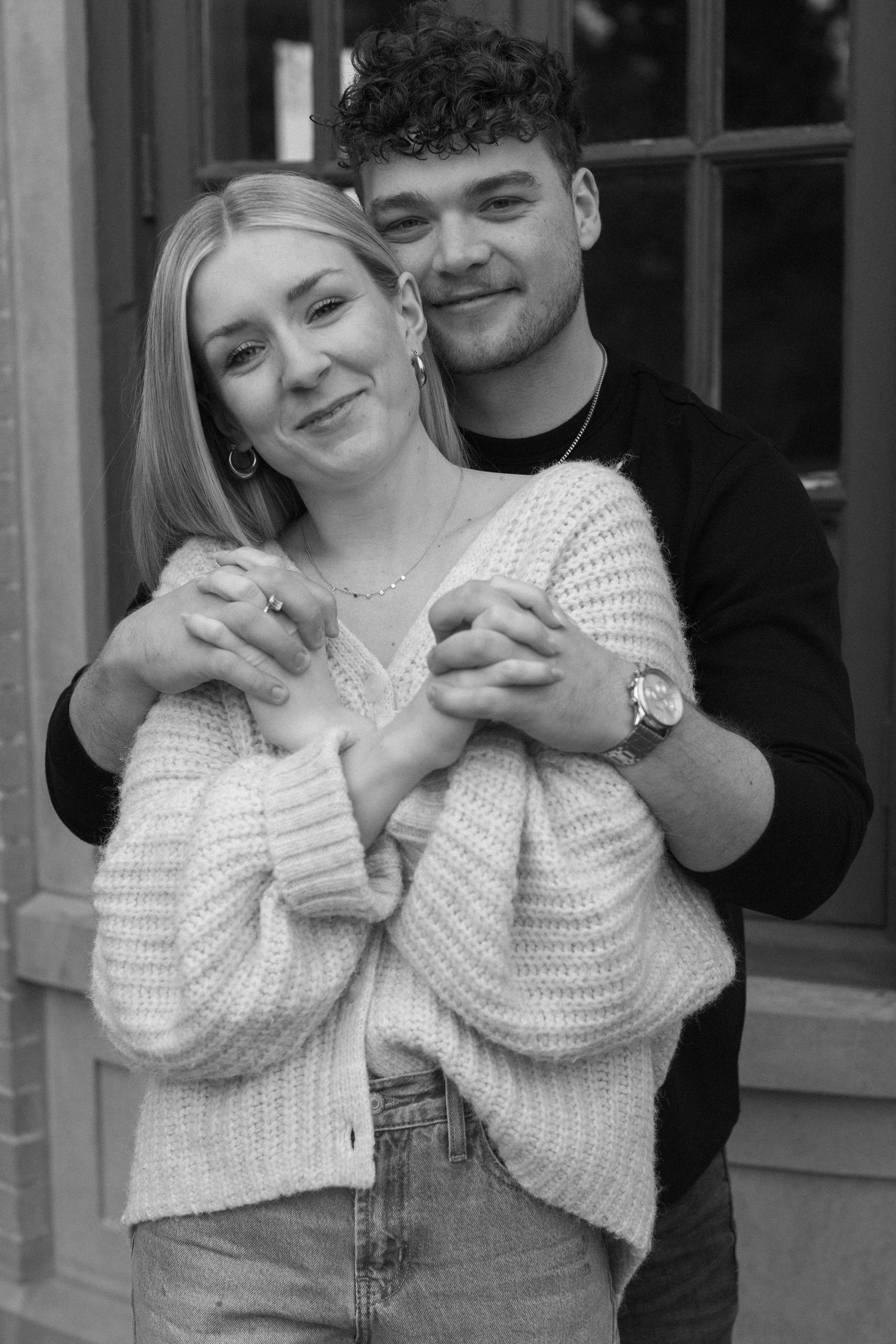 A couple embracing in black and white photography, wearing a white sweater and dark top.