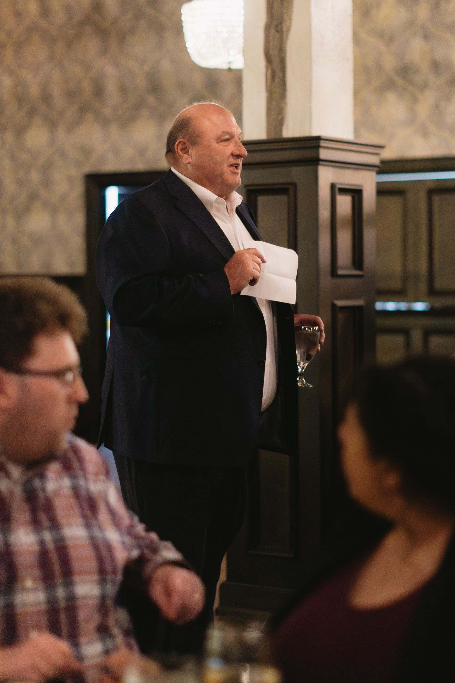 People gathered at formal event in elegant indoor venue with ornate wallpaper.