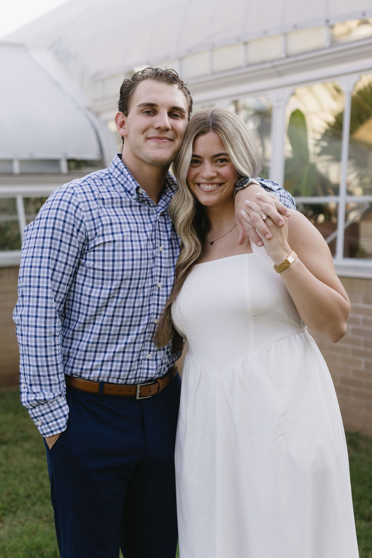 Happy couple poses together in semi-formal attire in front of a white building with arches.