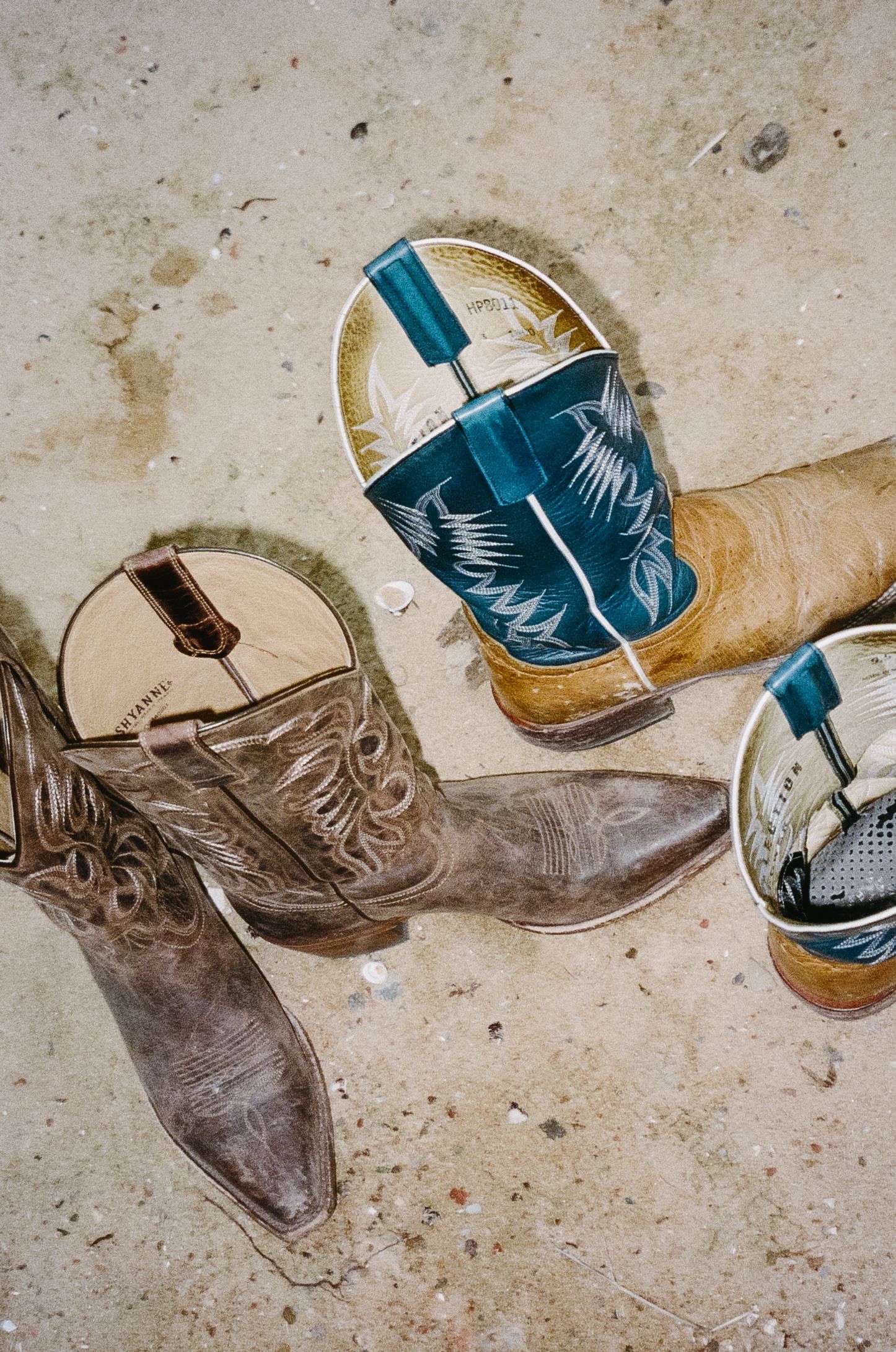 Vintage cowboy boots and decorative western tumblers arranged on a textured concrete surface.