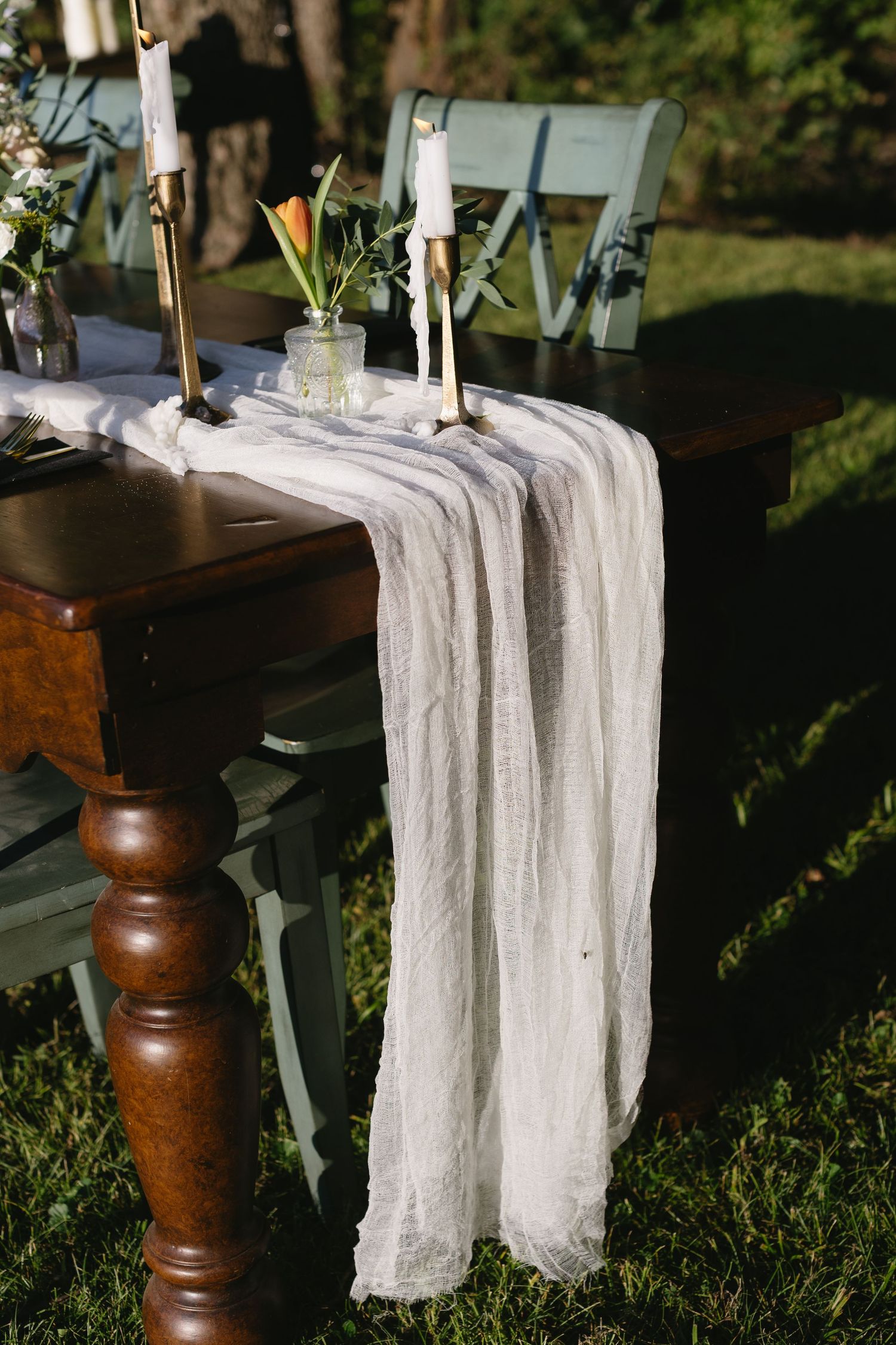 A vintage wooden table with white fabric runner and candlesticks set for a rustic outdoor wedding.