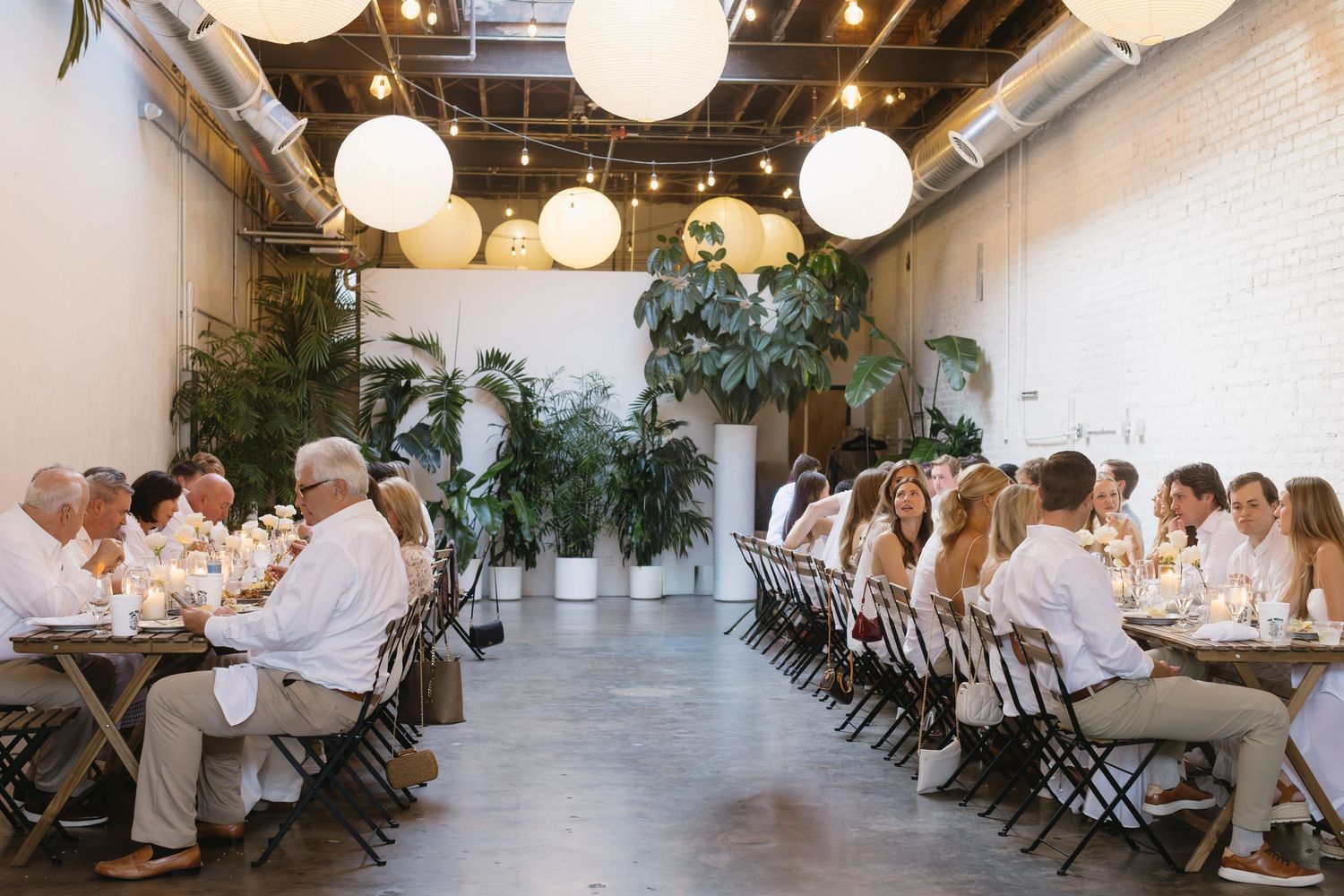 An elegant dinner reception setup with white paper lanterns and greenery decorations.