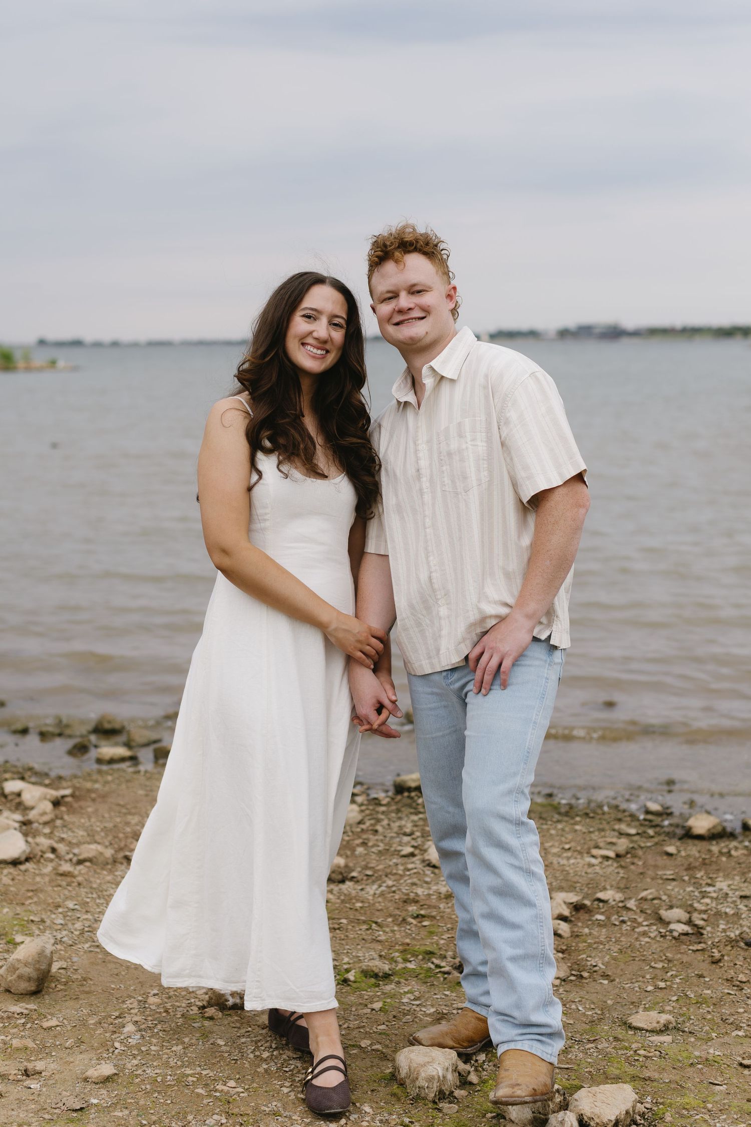 A couple shares tender moments on a rocky beach shoreline.