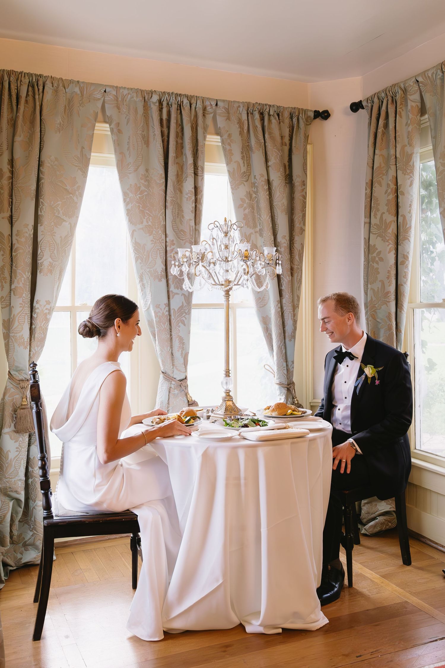 Elegant dining room with white tablecloths and floral curtains set for a wedding reception.
