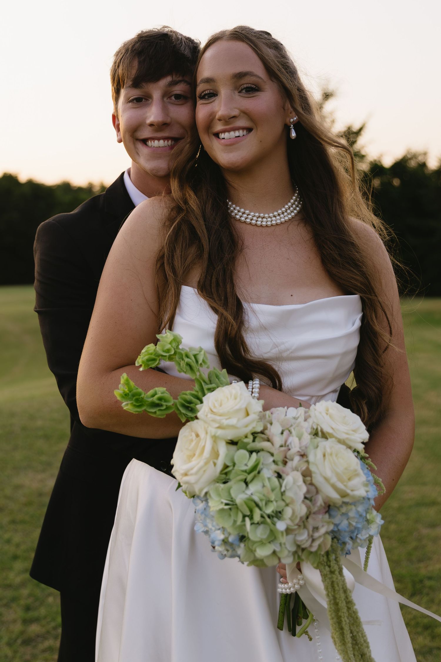 Candid wedding portraits of newlyweds at sunset with white rose bouquet.