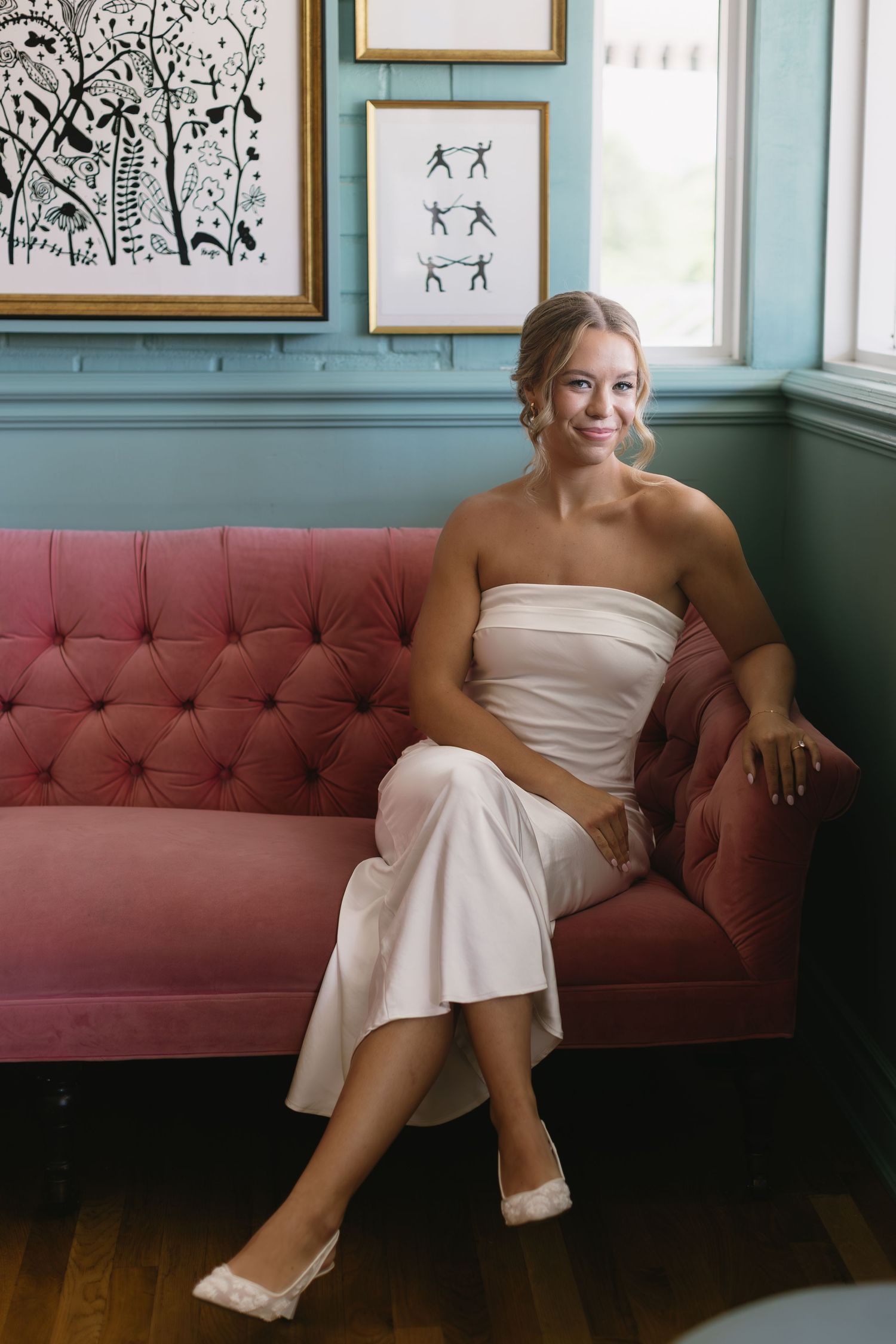 A relaxed moment on a pink couch with framed artwork and blue-green walls in the background.