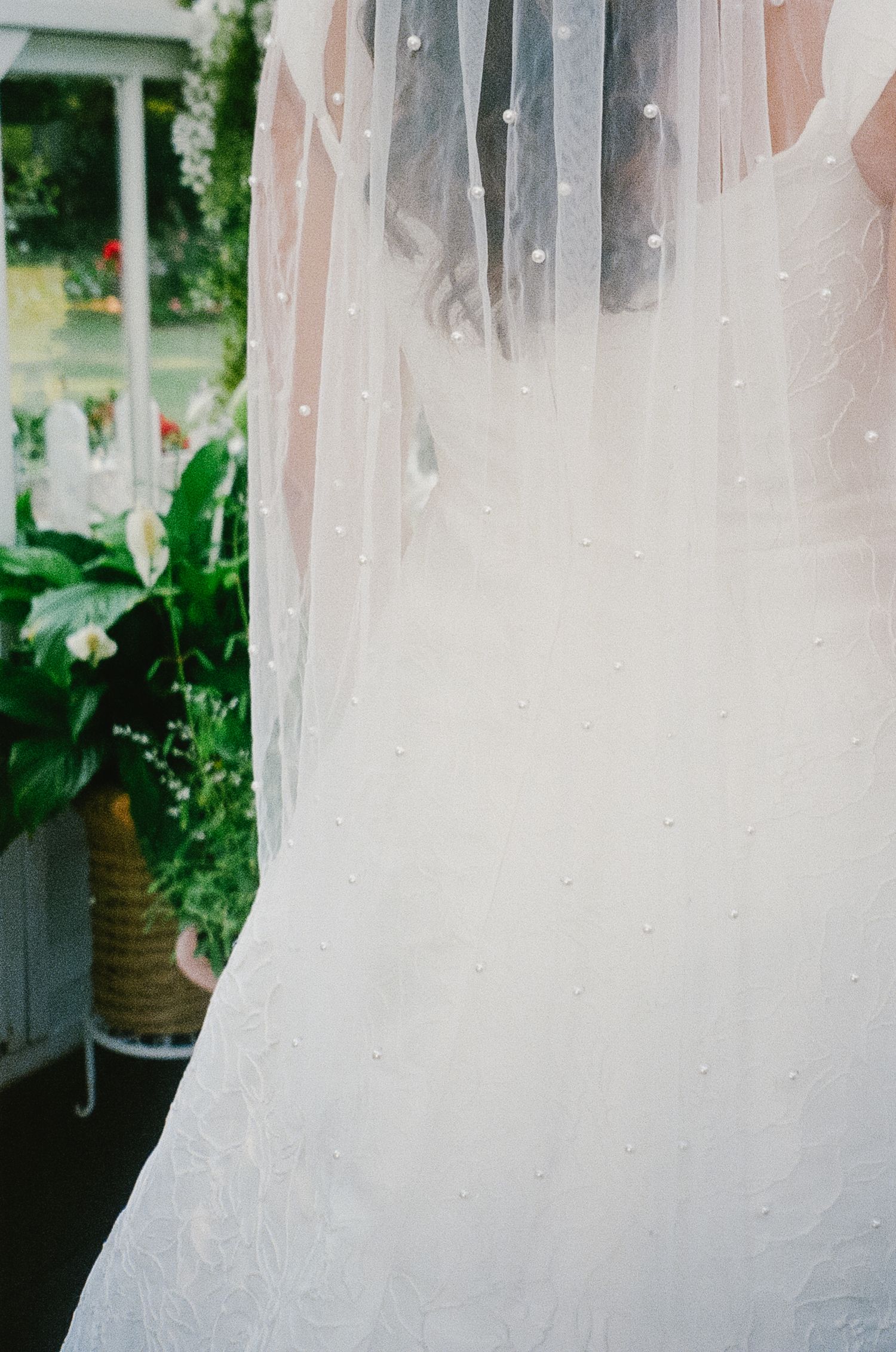 Detail shot of a flowing white wedding veil with delicate tulle fabric captured against a soft green garden background.