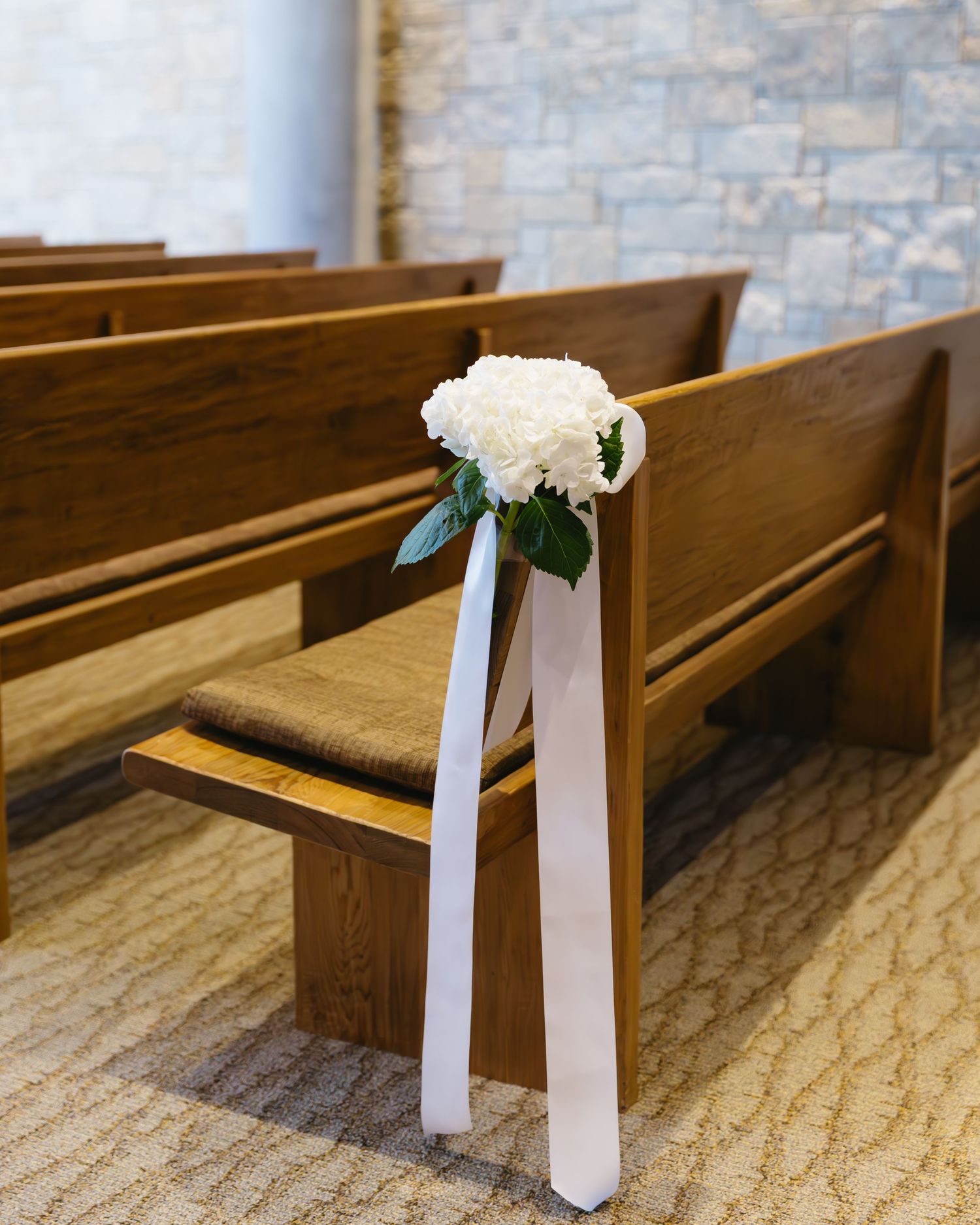 White ribbon and flower decorations adorn wooden church pews in sequence along a carpeted aisle.
