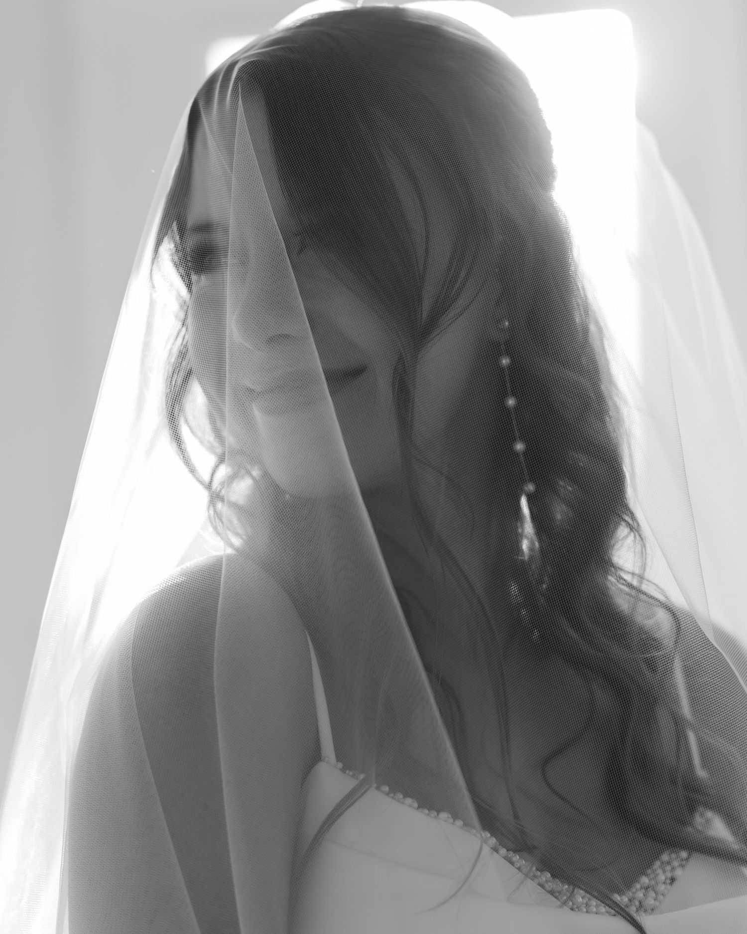 Black and white artistic portrait series of a bride with flowing veil in window light.