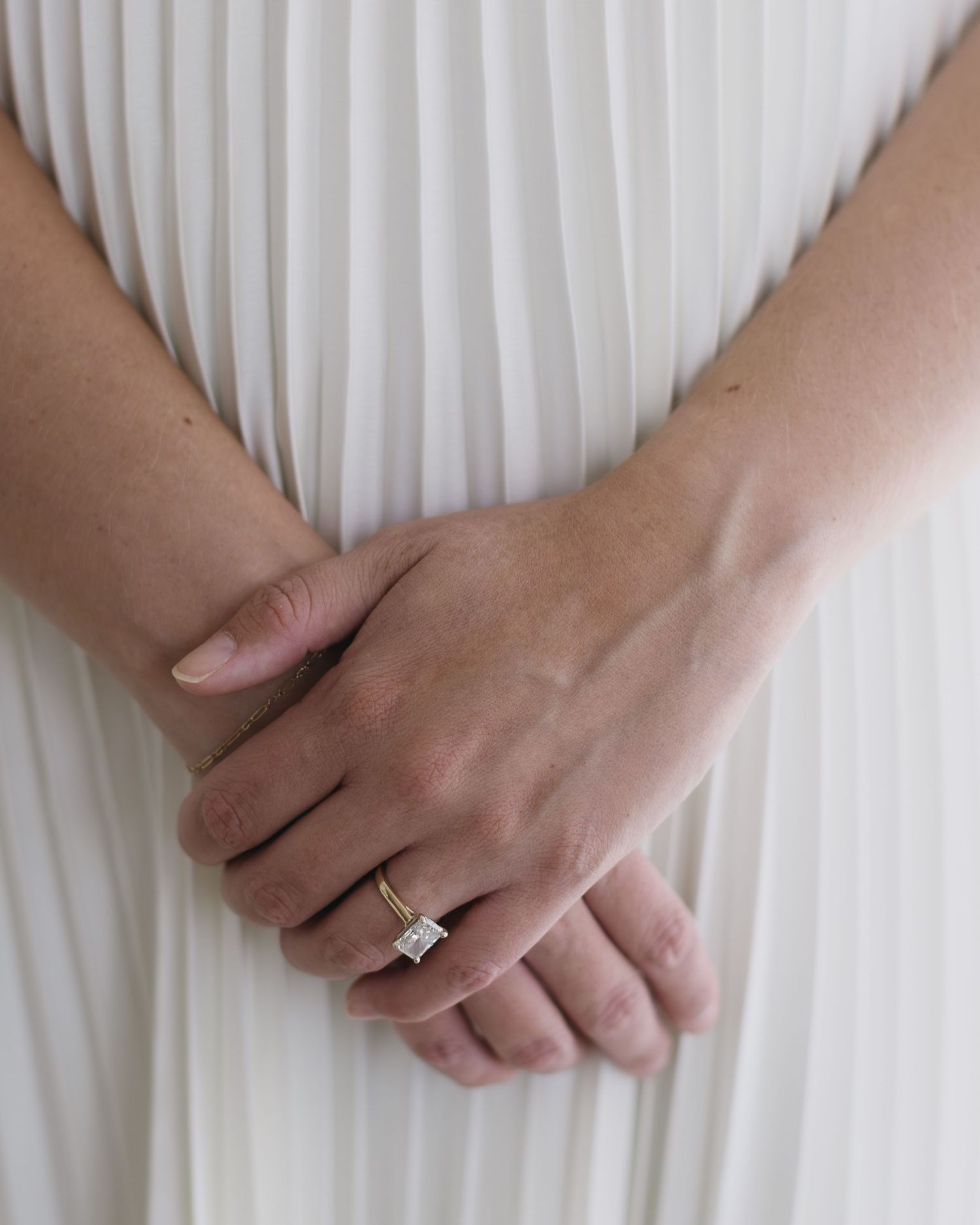 Close-up of hands in white pleated fabric showing diamond engagement ring.