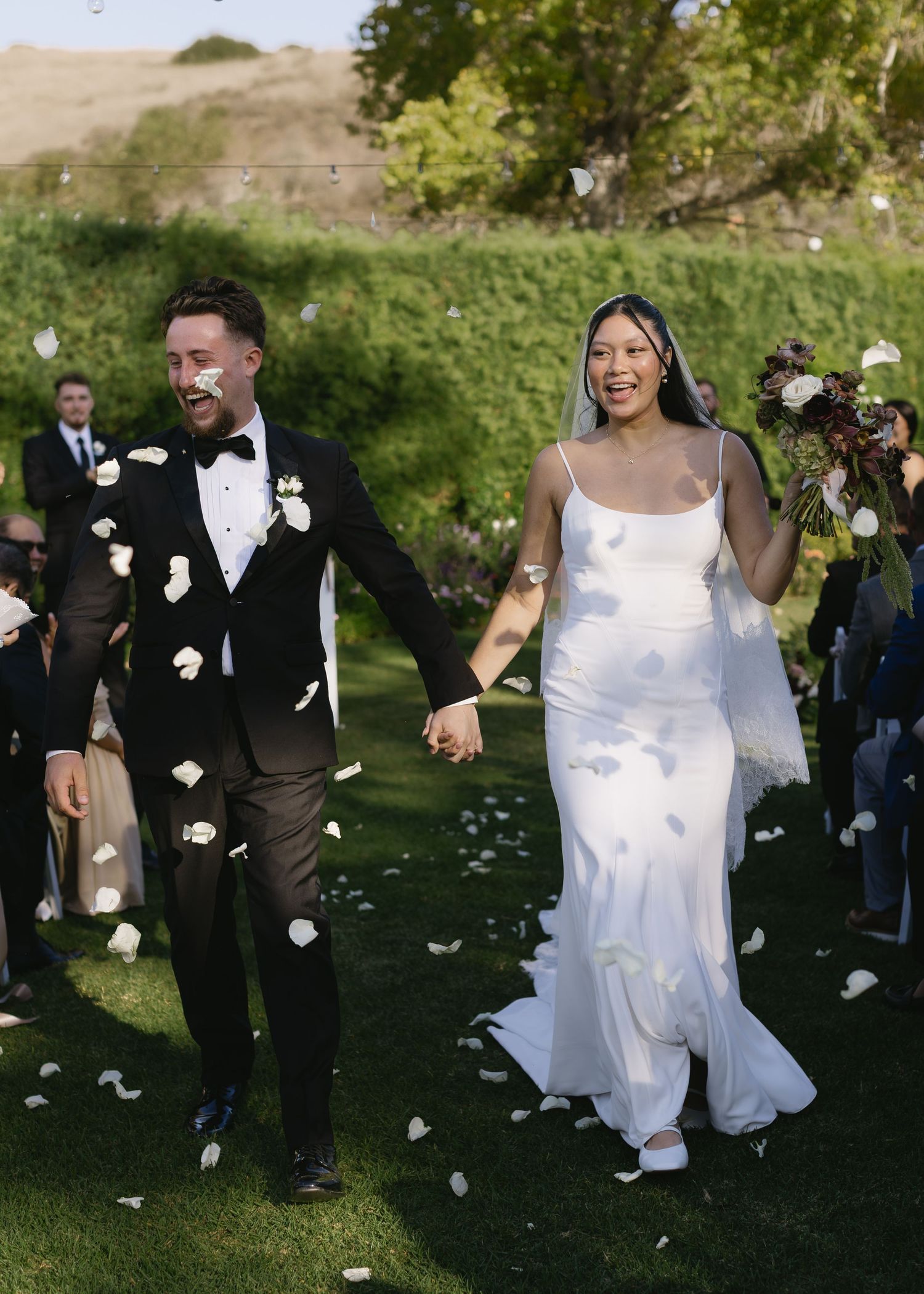 Wedding celebration with flower petals being tossed as couple walks through garden setting.