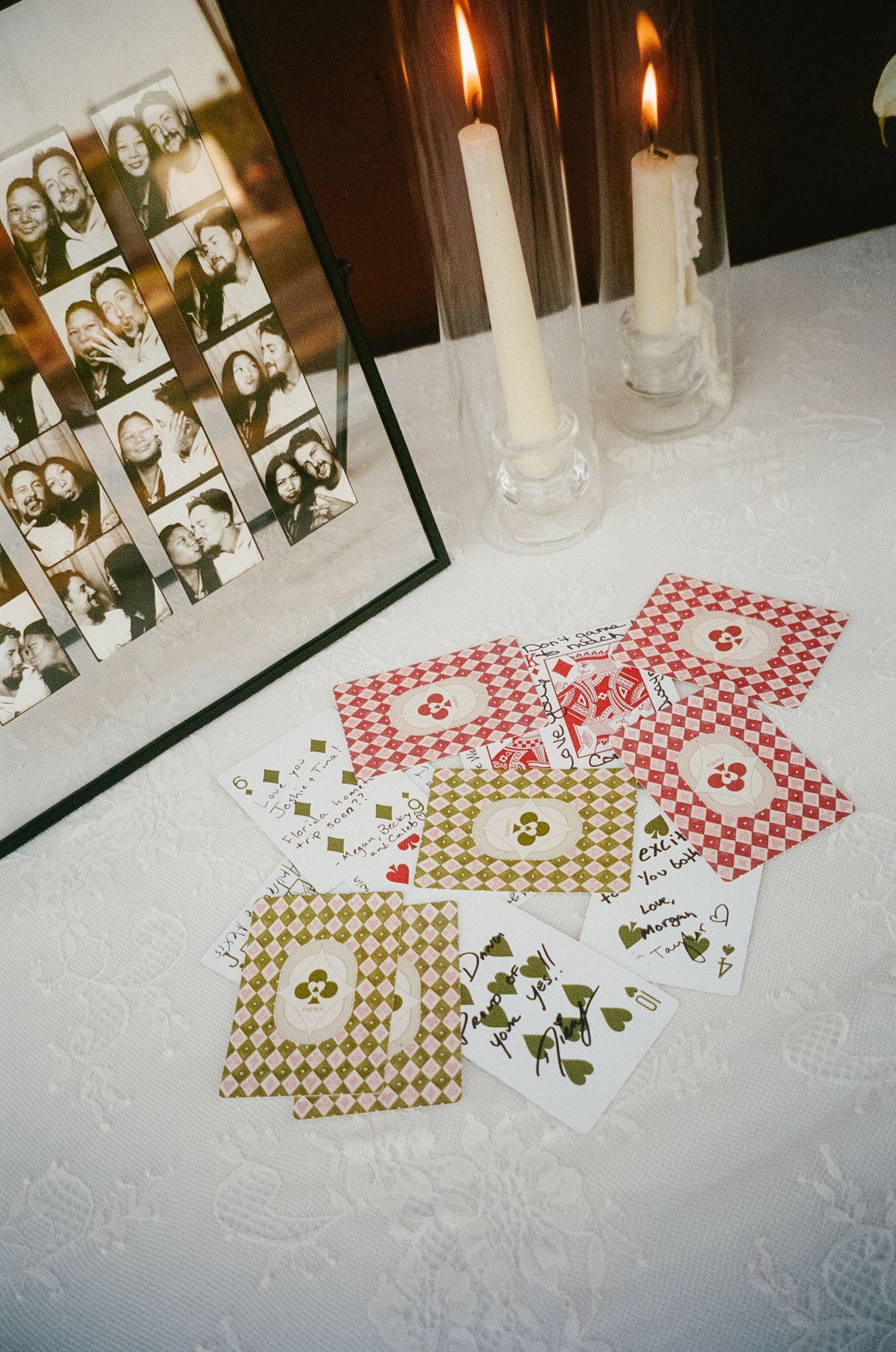 Playing cards and photographs arranged on a white tablecloth with lit candles creating an intimate atmosphere.