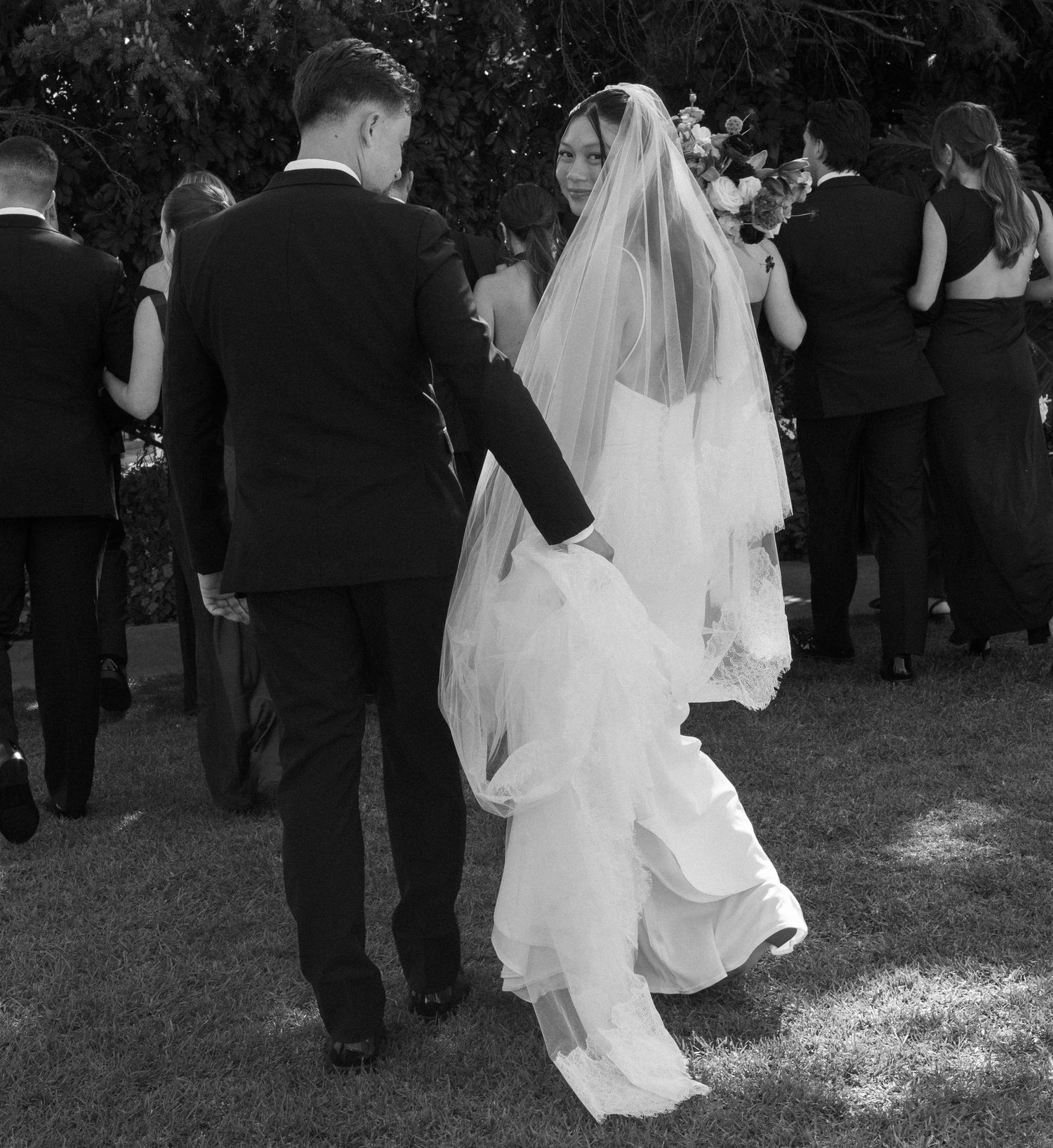 A black and white photo of a couple walking together during their outdoor wedding ceremony.
