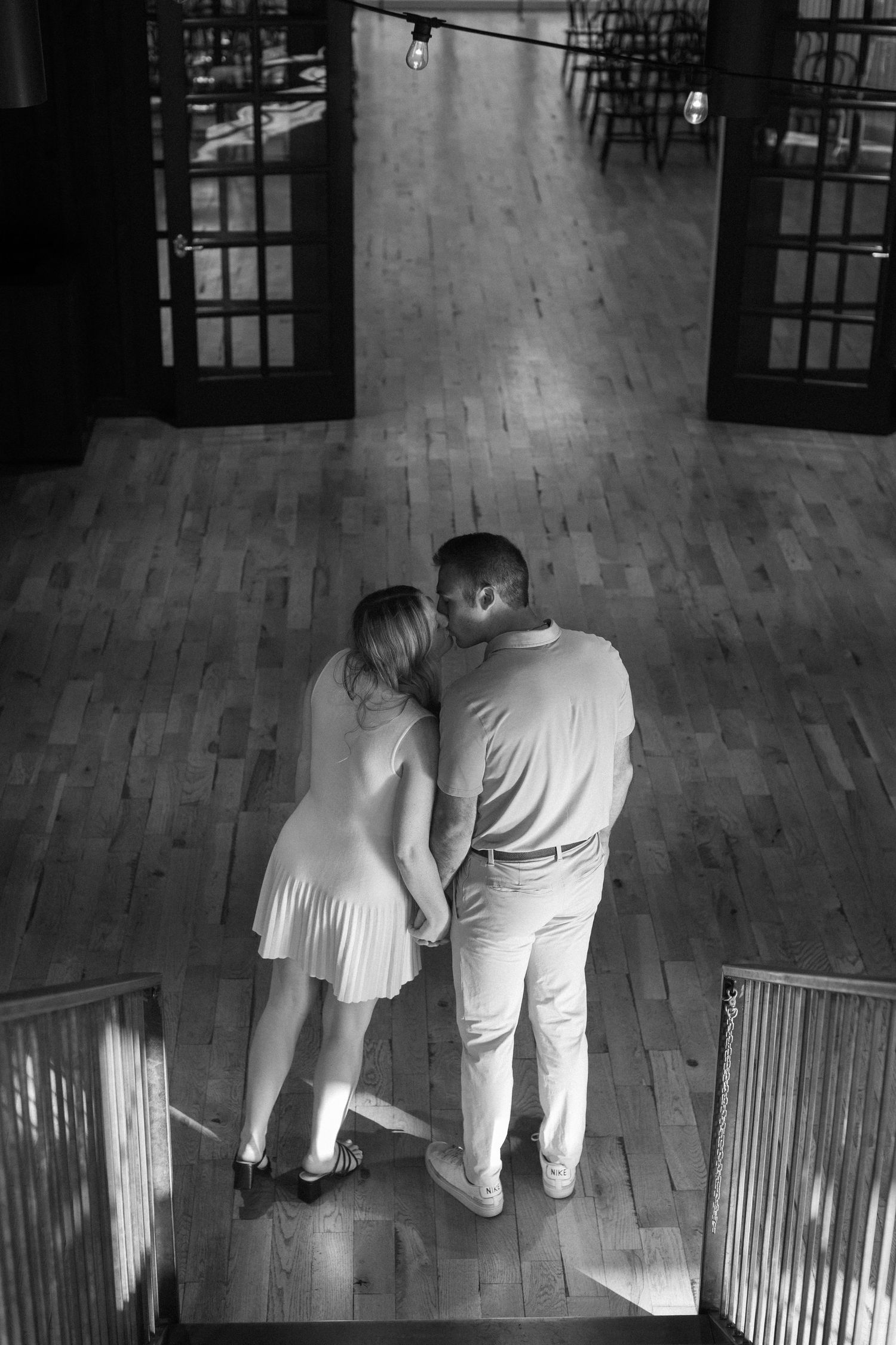 A couple dances together on a hardwood floor in a dimly lit room with windows.