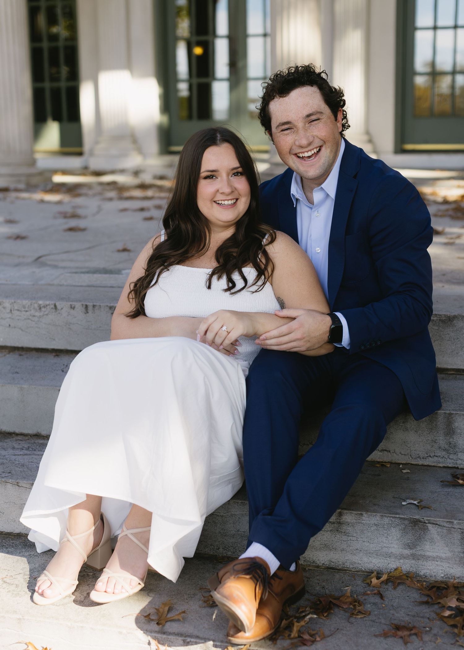 A couple in formal wear sits and laughs together on stone steps.