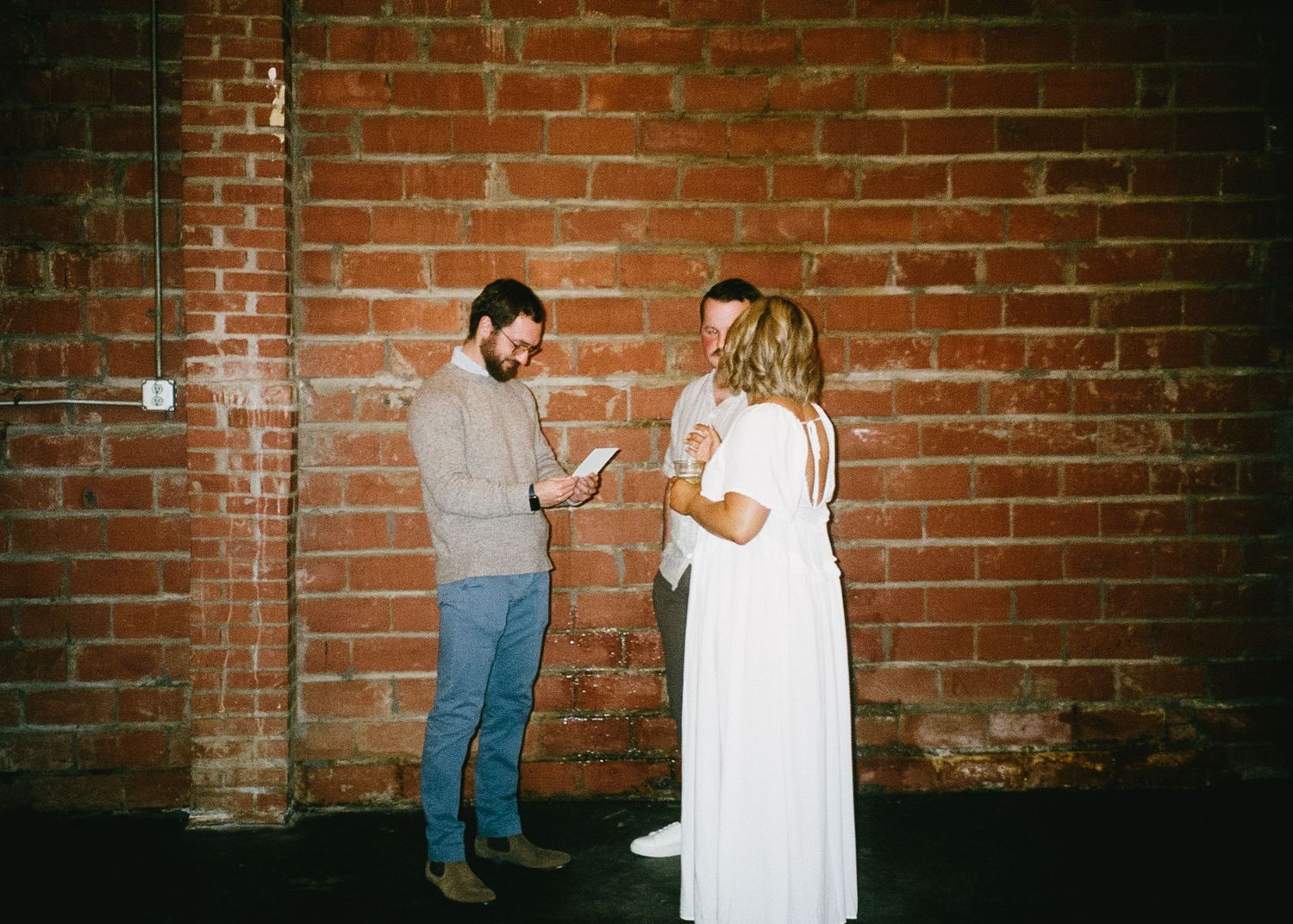 Couple sharing a playful moment against an exposed brick wall at an event.