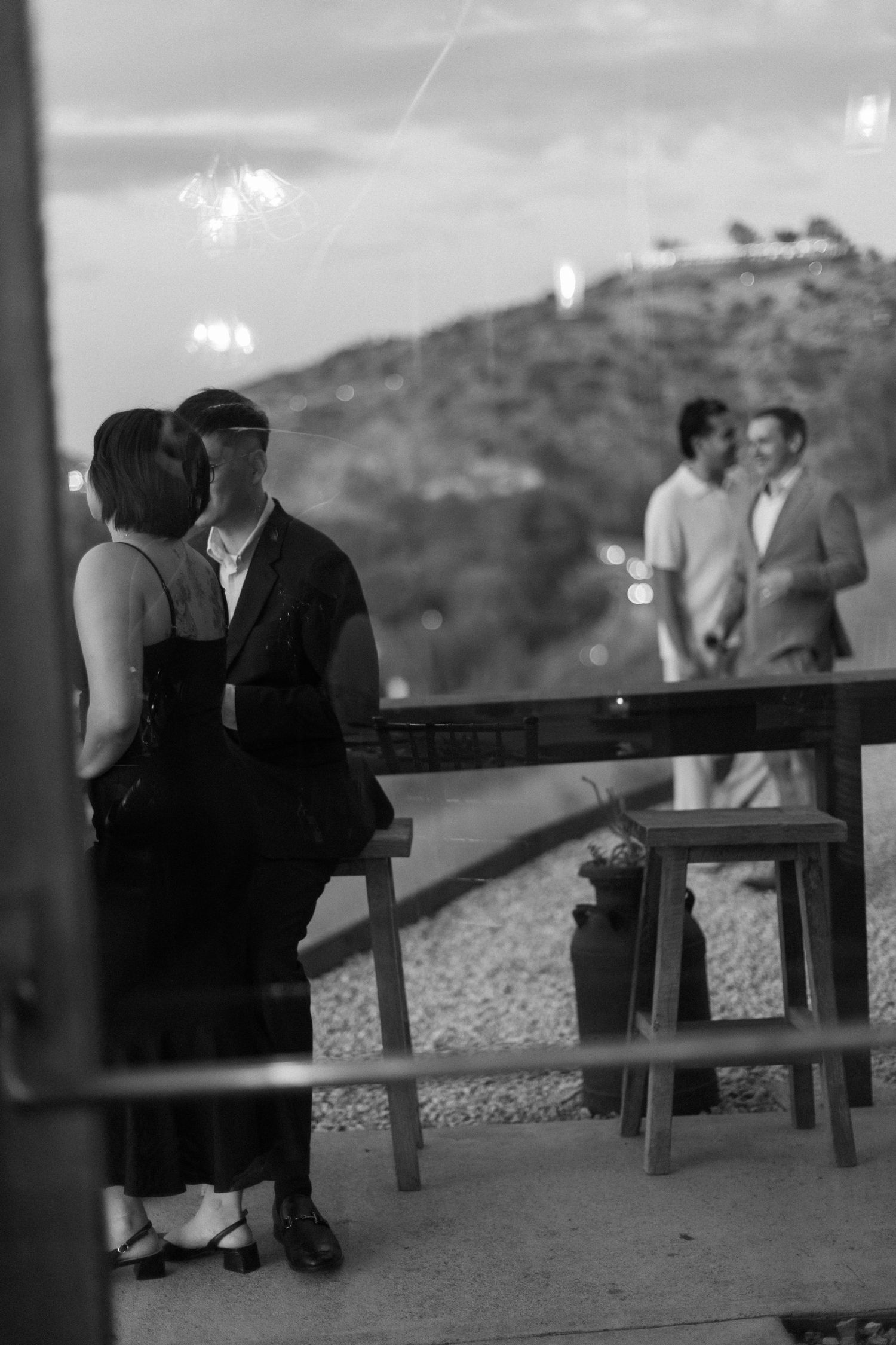 Black and white photo of wedding guests mingling on an outdoor terrace with mountain views.