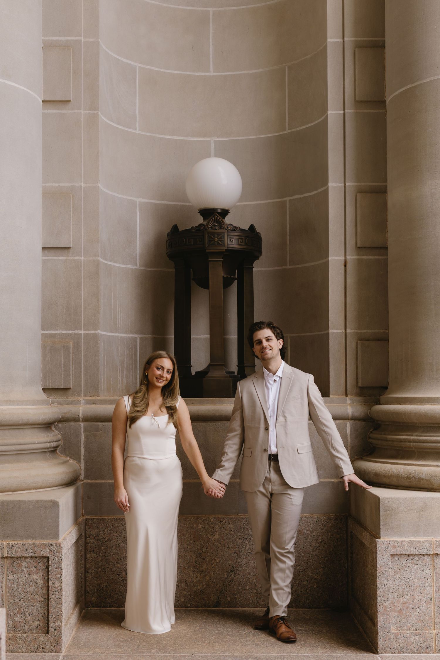 A couple in matching neutral tones poses elegantly against classical stone columns.
