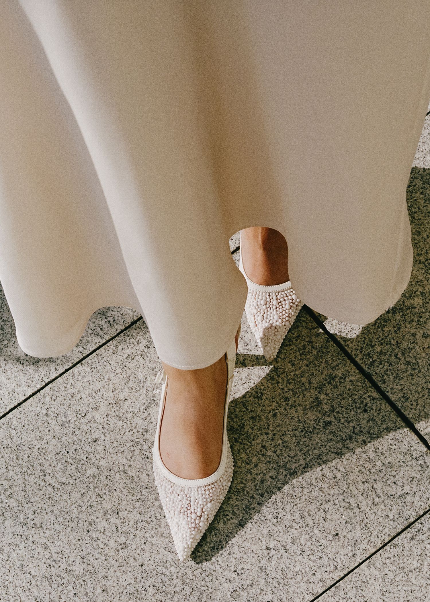 Close-up of delicate white lace bridal shoes on a textured stone floor.