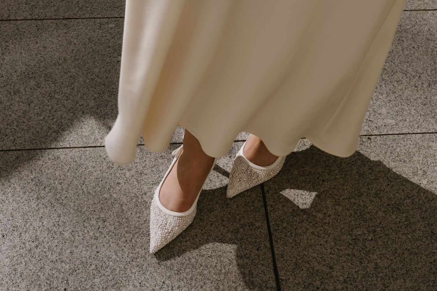 Close-up view of formal white shoes and dress hem against stone steps.