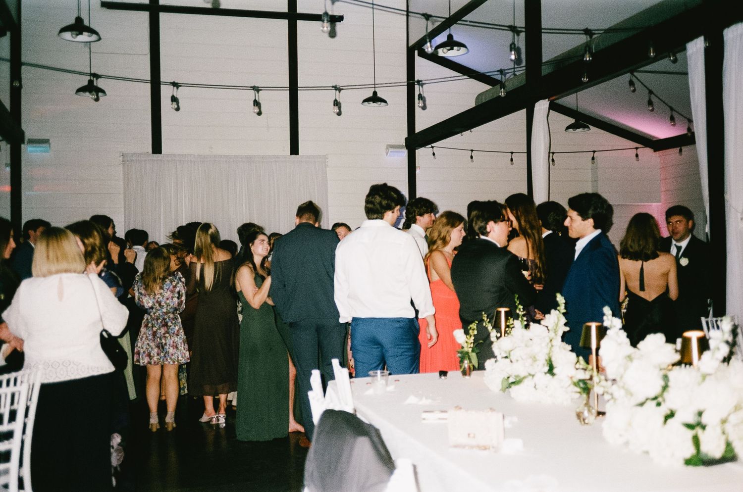 Wedding reception venue with string lights and elegant table settings visible in the background.