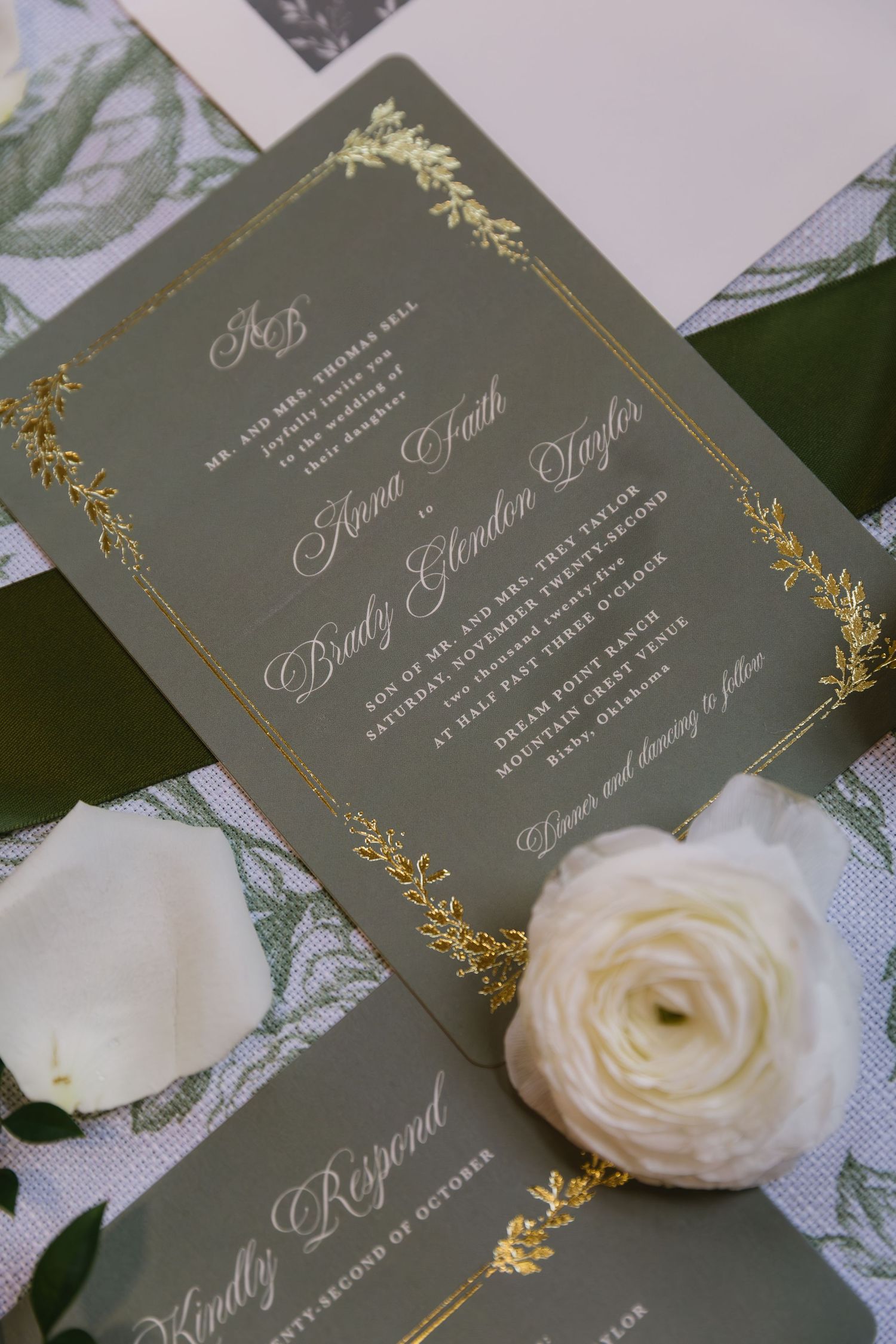 Elegant gray wedding invitations with gold foil accents and white ranunculus flowers on lace background.