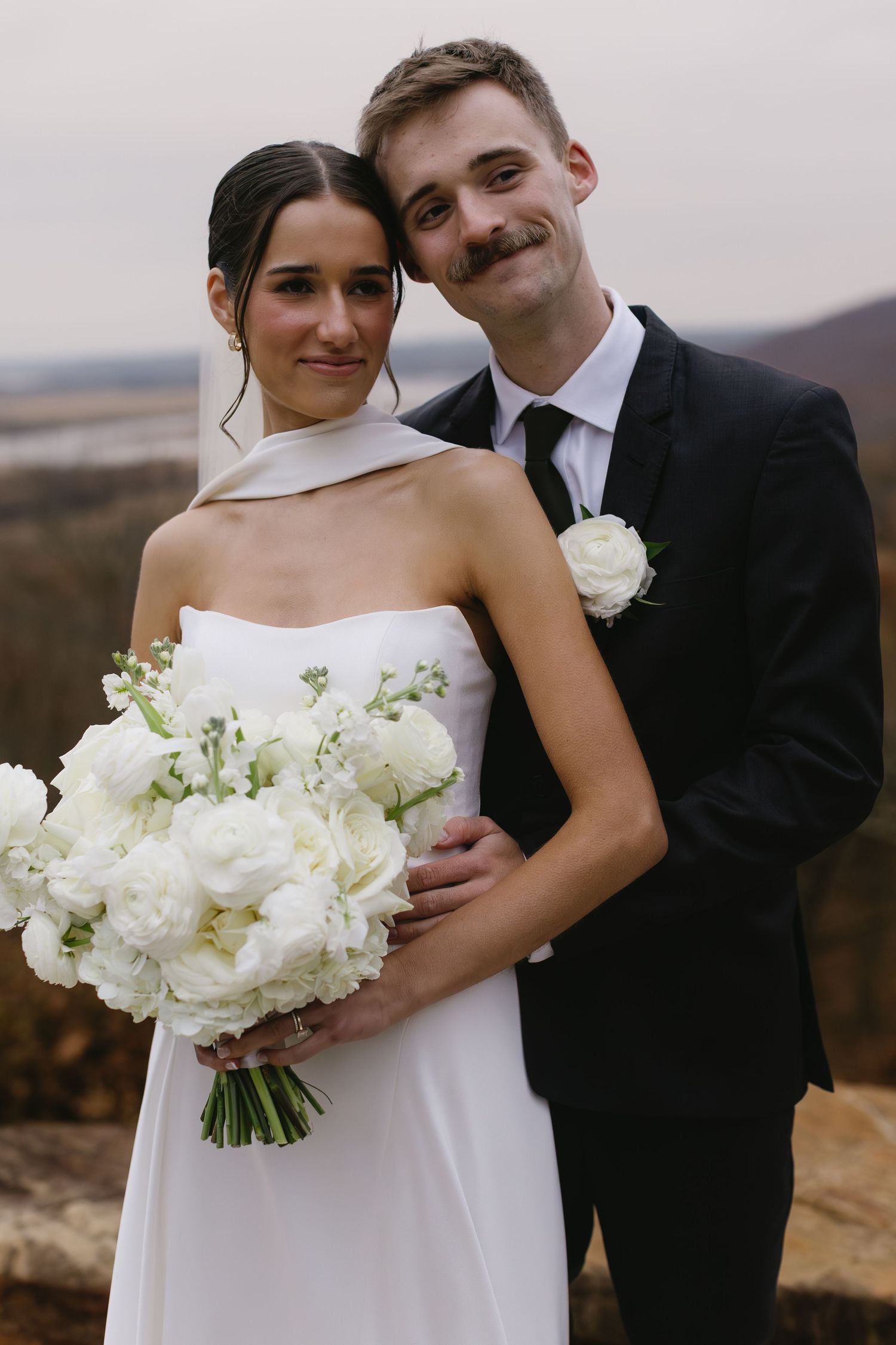 Classic wedding portrait featuring white bouquet and elegant attire against autumn landscape.