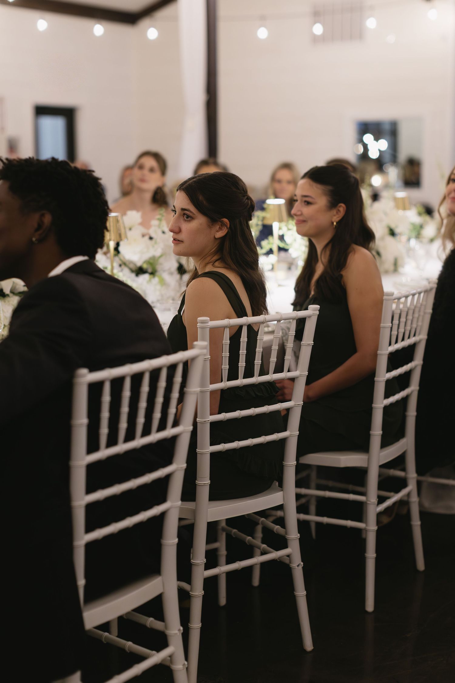 Wedding reception guests seated at elegant white chiavari chairs in a formal dining setting.