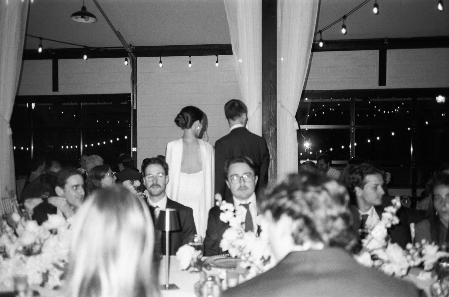 Wedding reception venue with string lights and guests seated at decorated tables.
