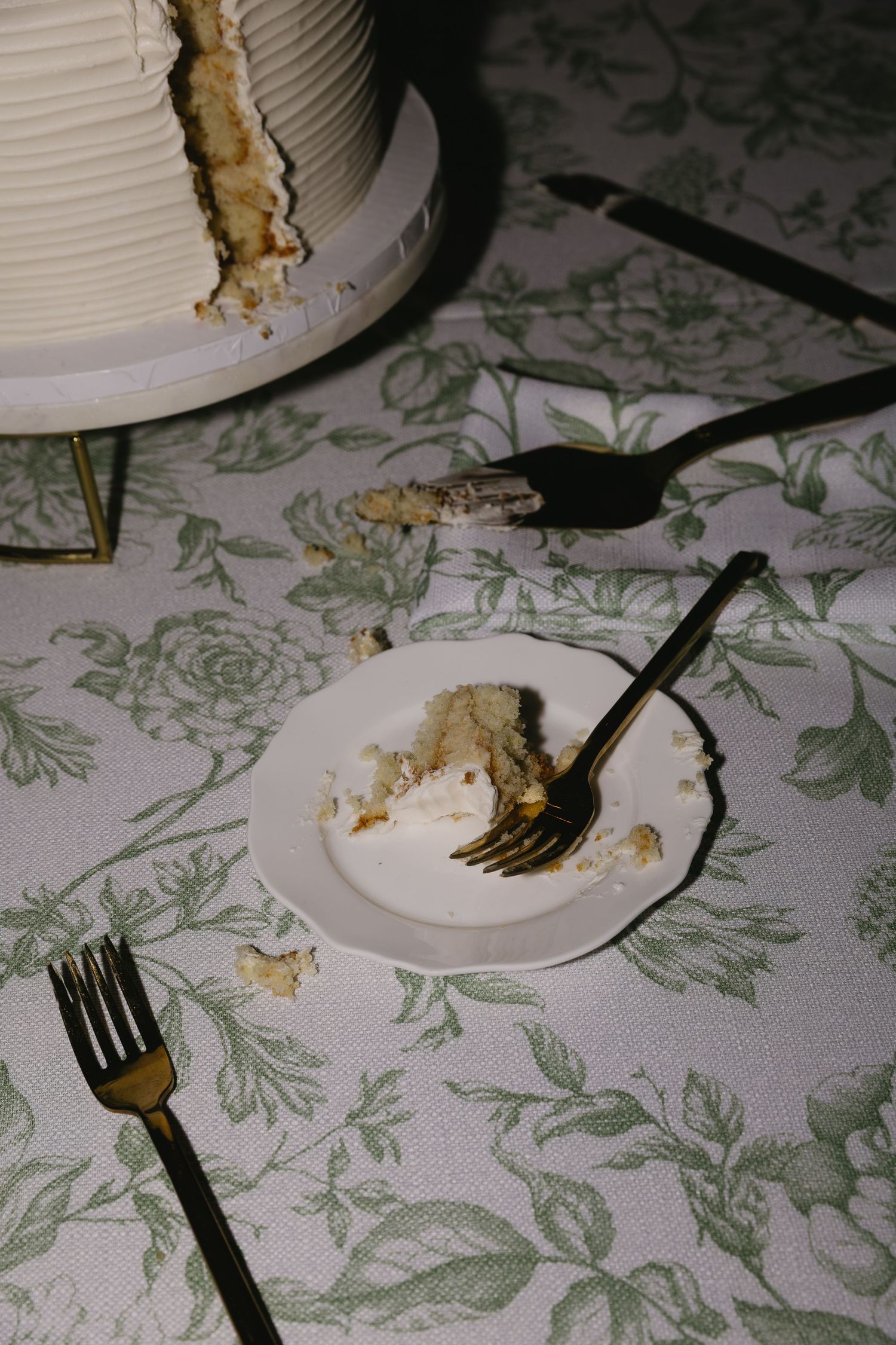 Partially eaten wedding cake with forks on a floral patterned tablecloth.