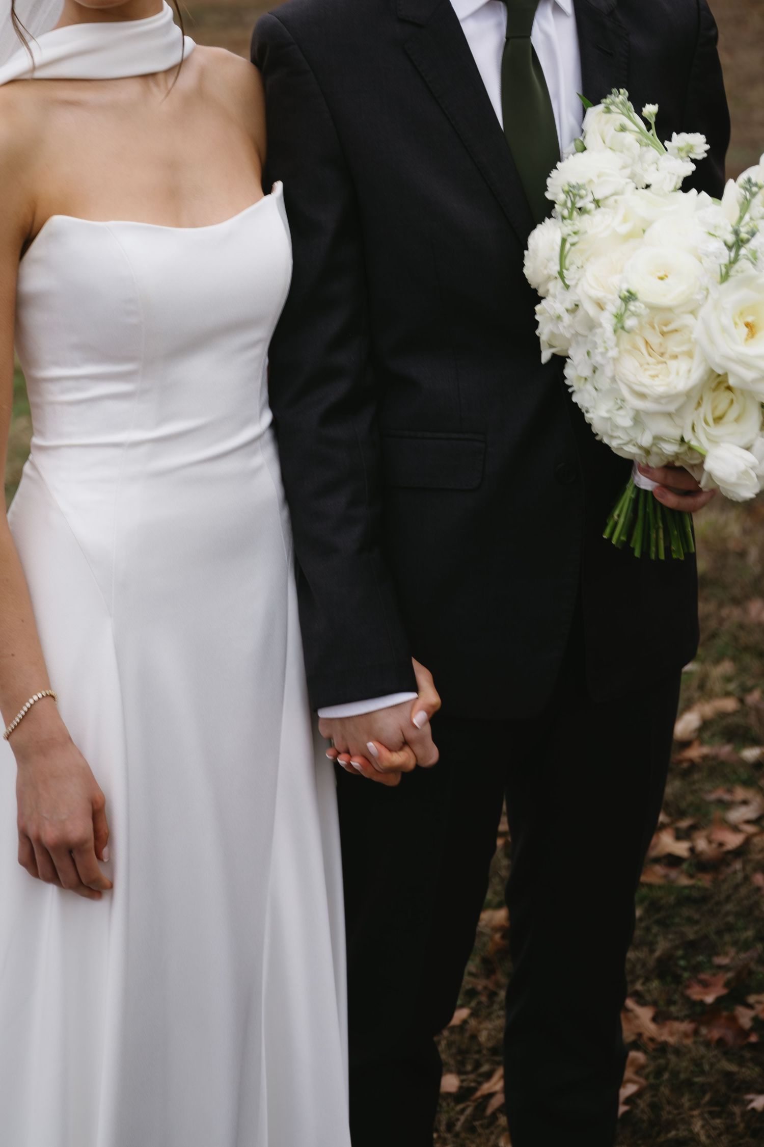 Elegant wedding couple in classic black and white attire holding hands with white floral bouquet.