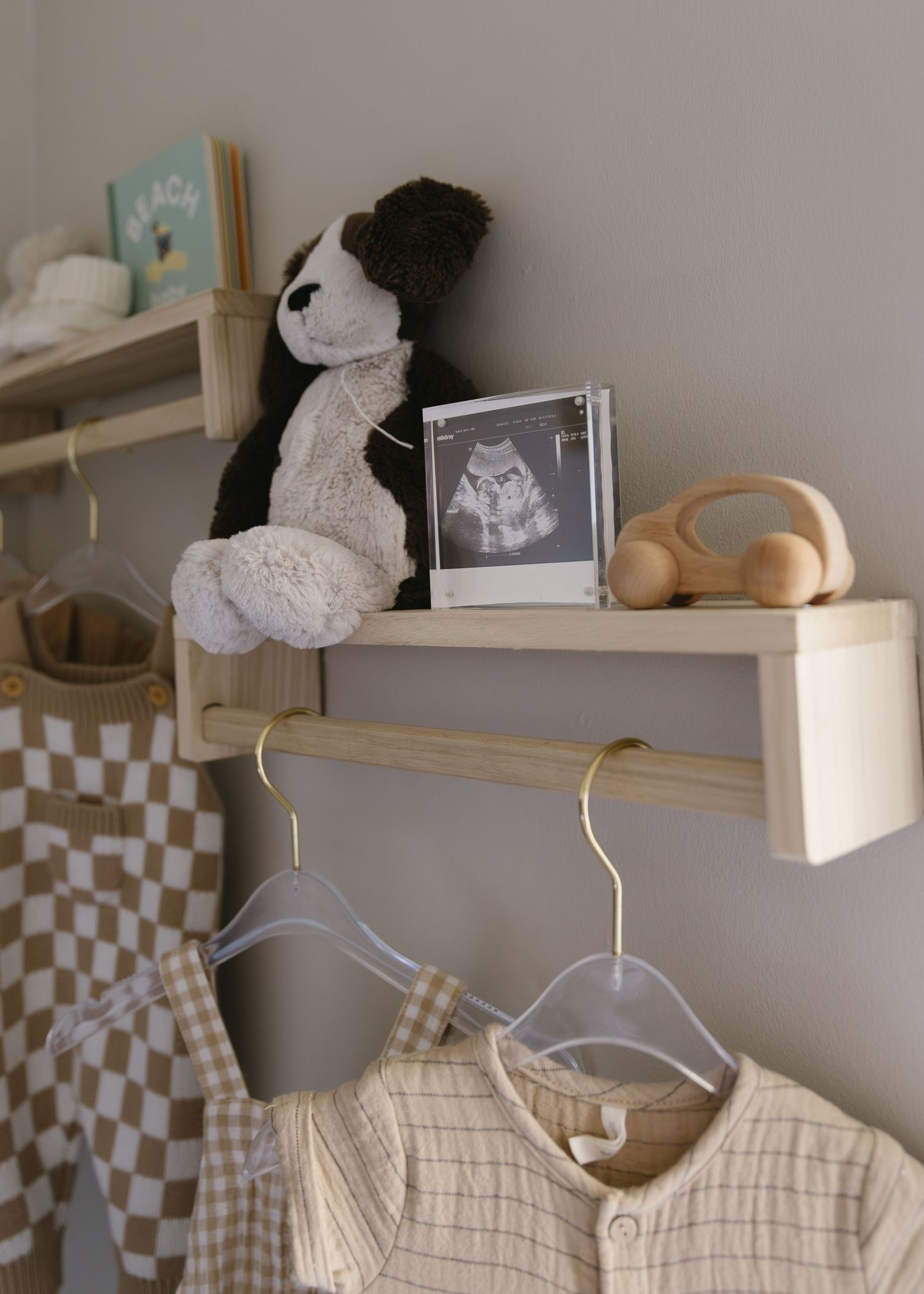Nursery shelf displaying baby clothes and stuffed animals in neutral tones.