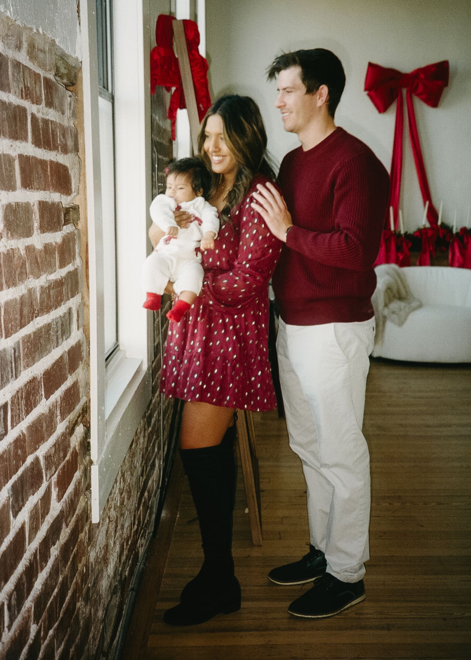 A family poses for holiday photos in coordinated burgundy and white outfits near a decorated window.