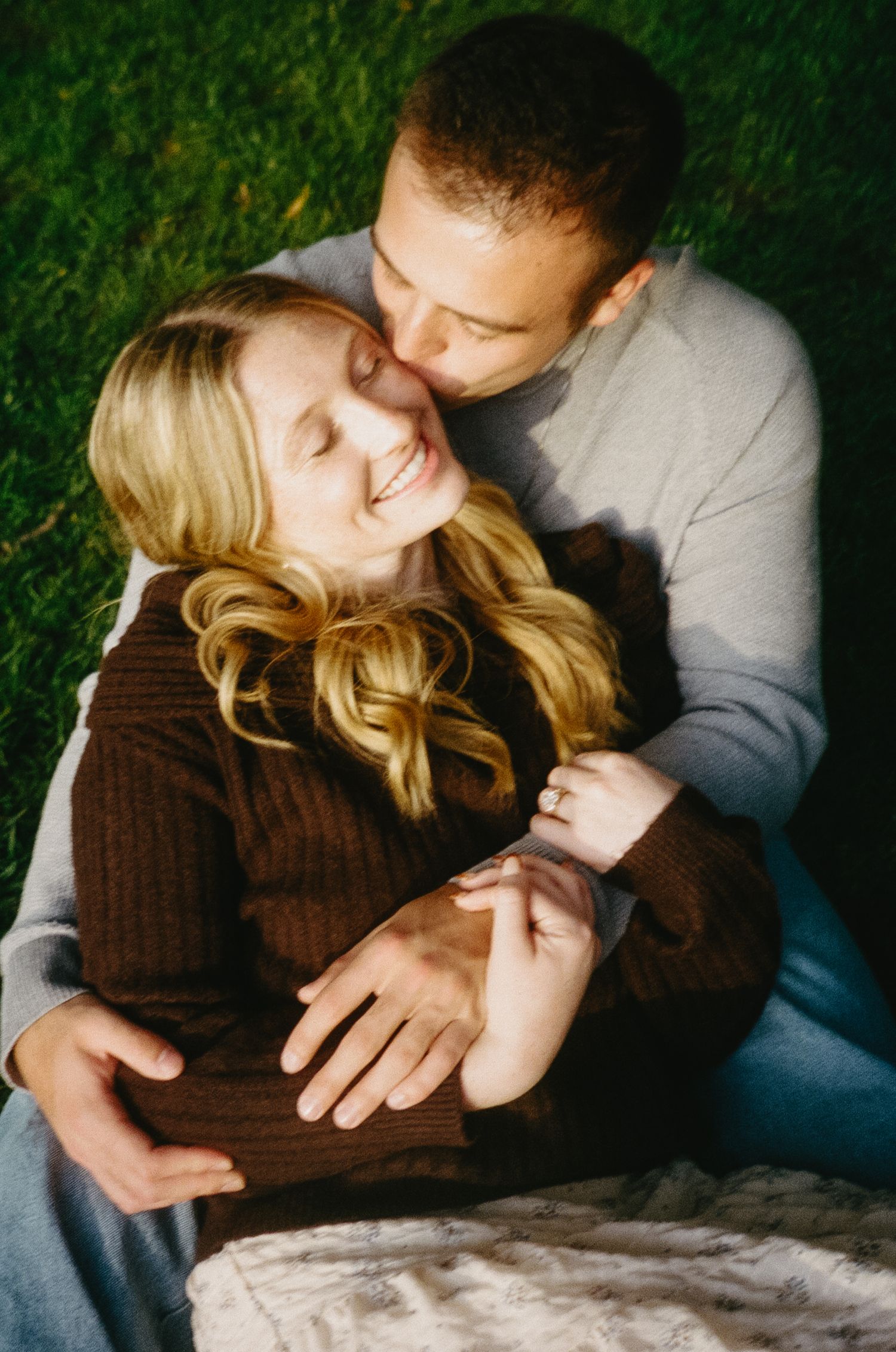 Couple lying together on blanket in grass during outdoor photoshoot.