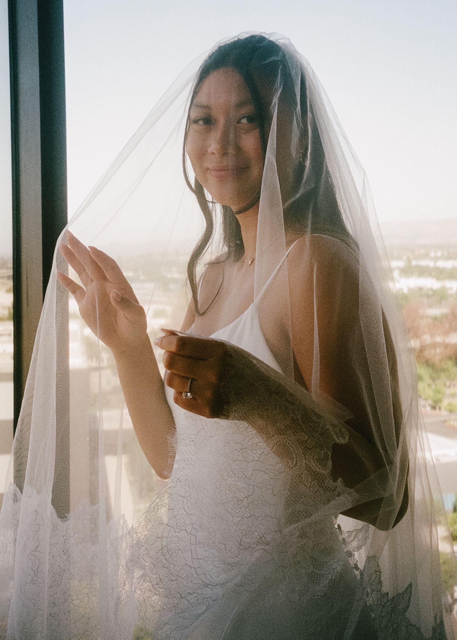 Elegant bridal portrait by window showing lace veil and white wedding dress.