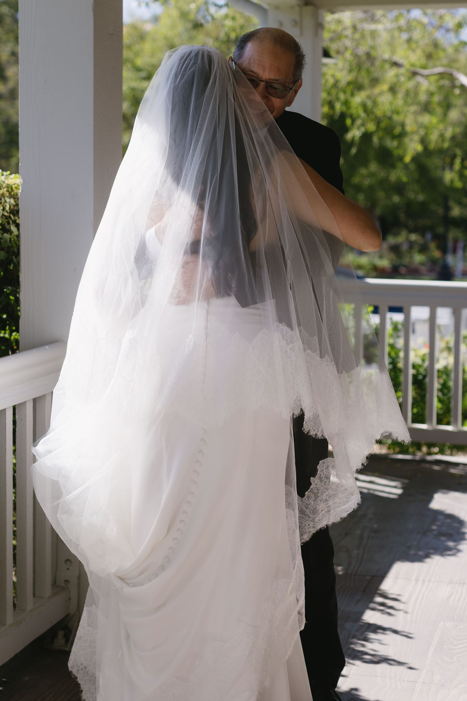 Newlyweds share tender moments on a covered porch with sunlight streaming through.