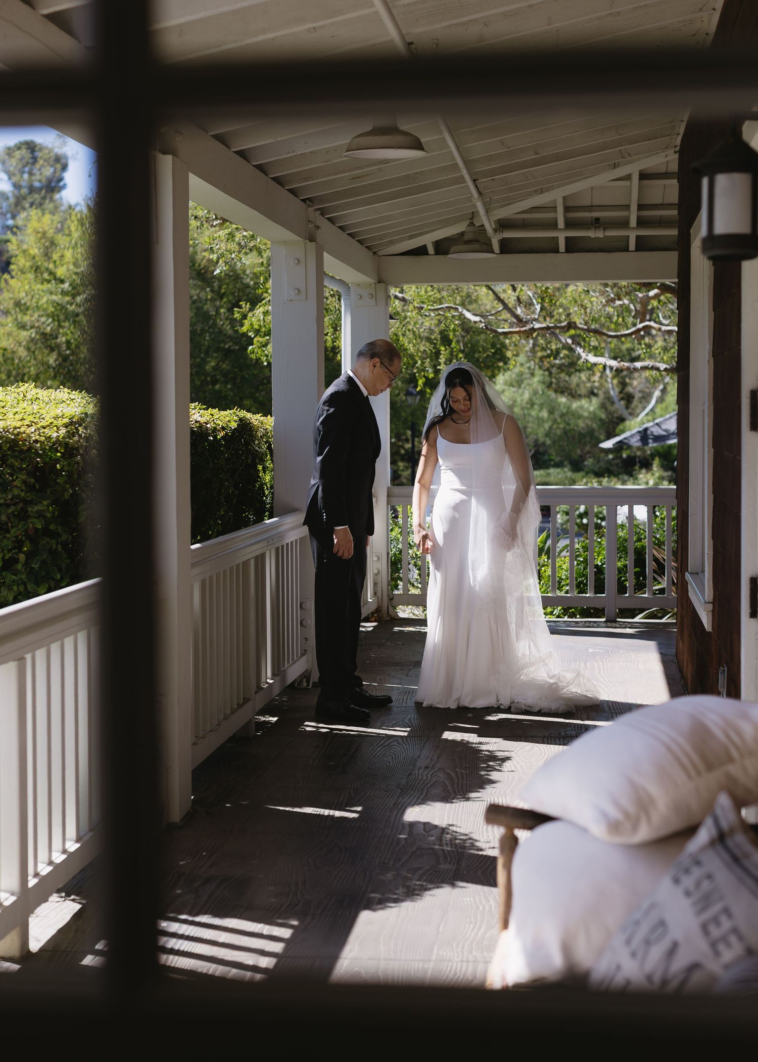 Couple walking along a covered porch walkway with sunlight streaming through the columns.