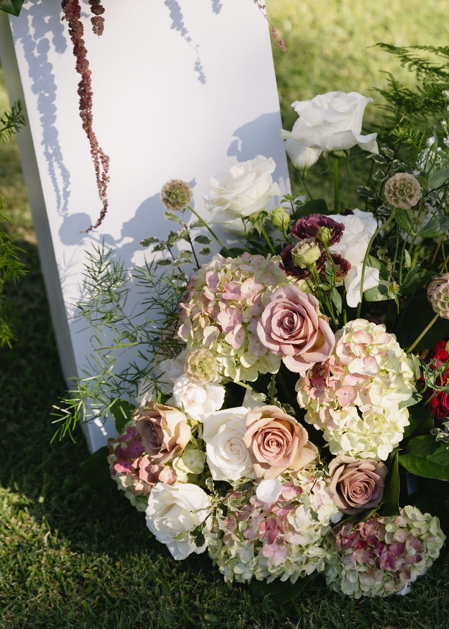 Beautiful floral arrangement with pink roses and hydrangeas decorates white wedding backdrop.