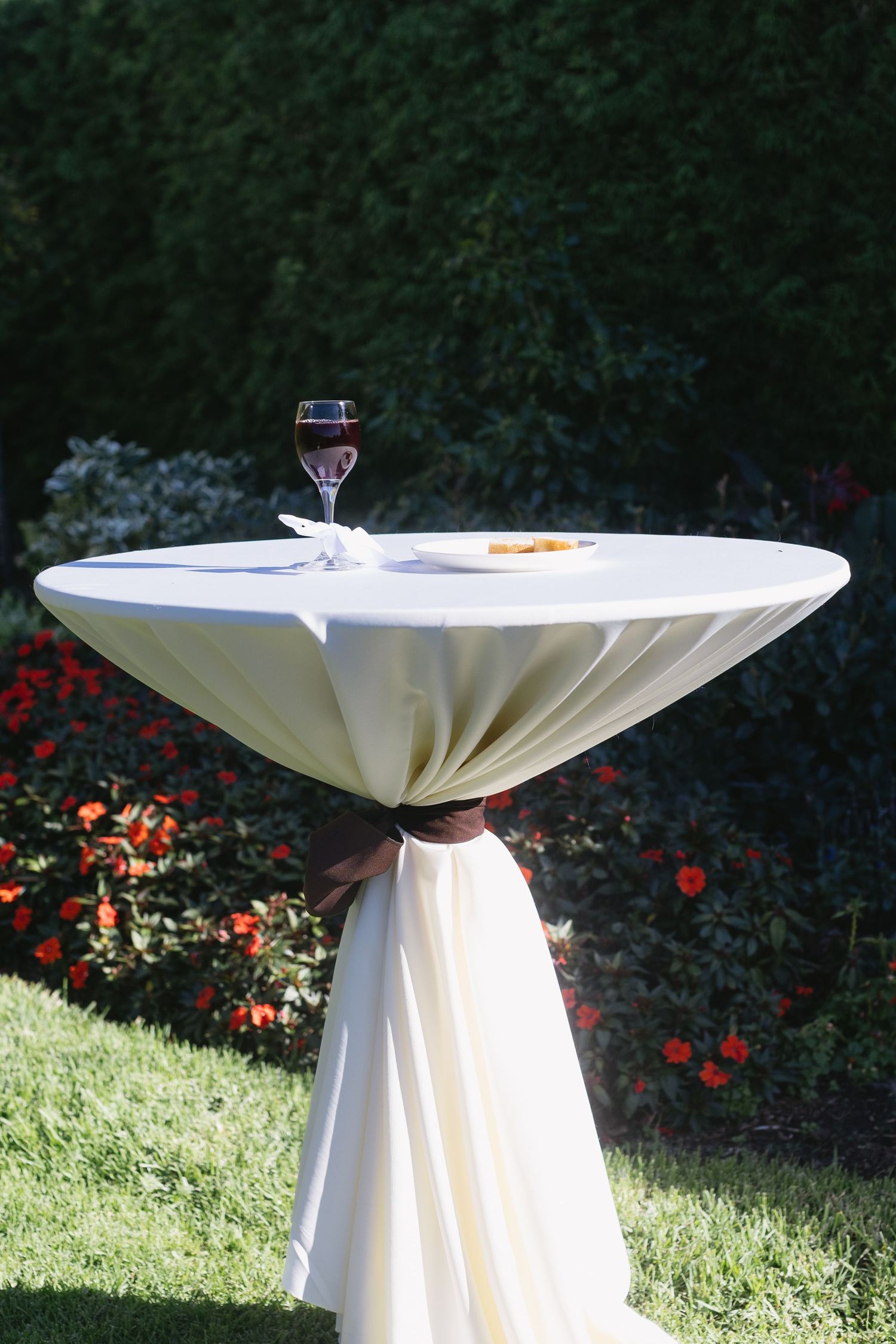 White cocktail tables with pleated linens arranged outdoors for an elegant garden reception.